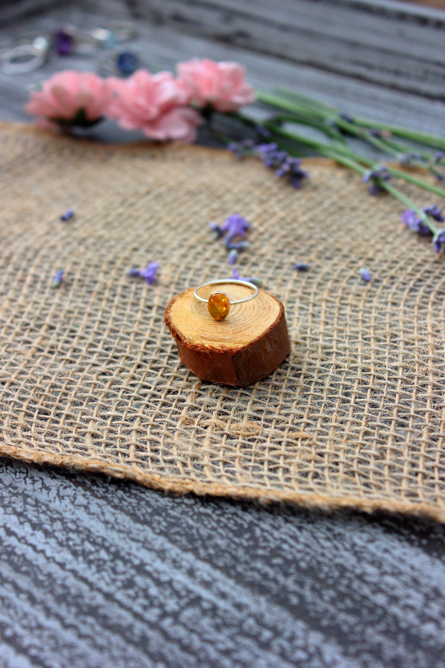 Ring with a yellow gemstone on a wooden block, surrounded by flowers on a textured surface