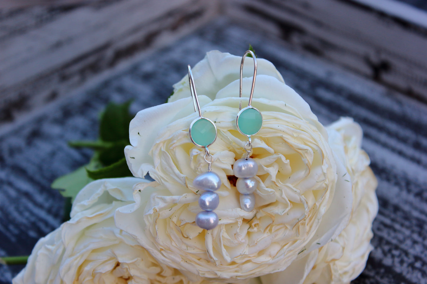 Pearl and blue gemstone earrings on a white rose
