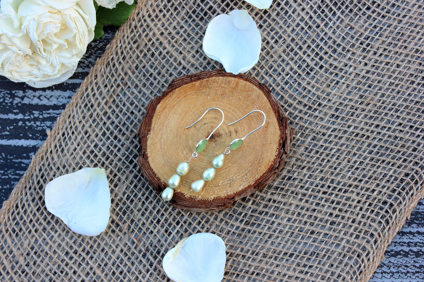 Pearl earrings on a wooden slice with white flowers on a textured surface