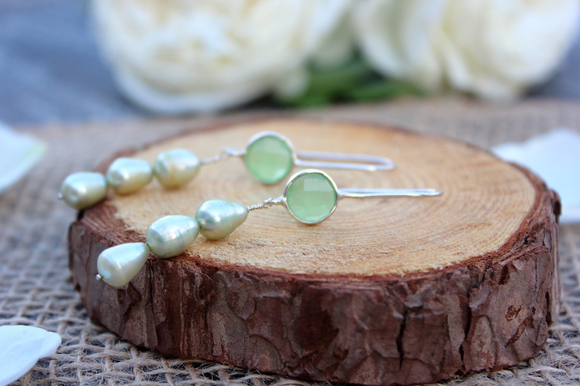 Pair of earrings with green pearls on a wooden surface with flowers in the background
