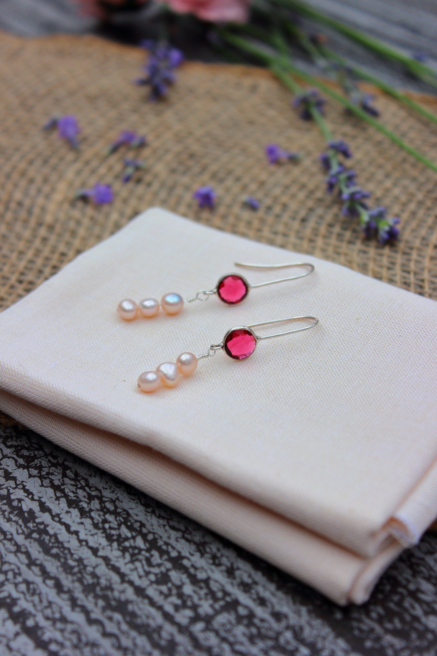 Pair of earrings with pink and pearl-like stones on a white cloth with flowers in the background