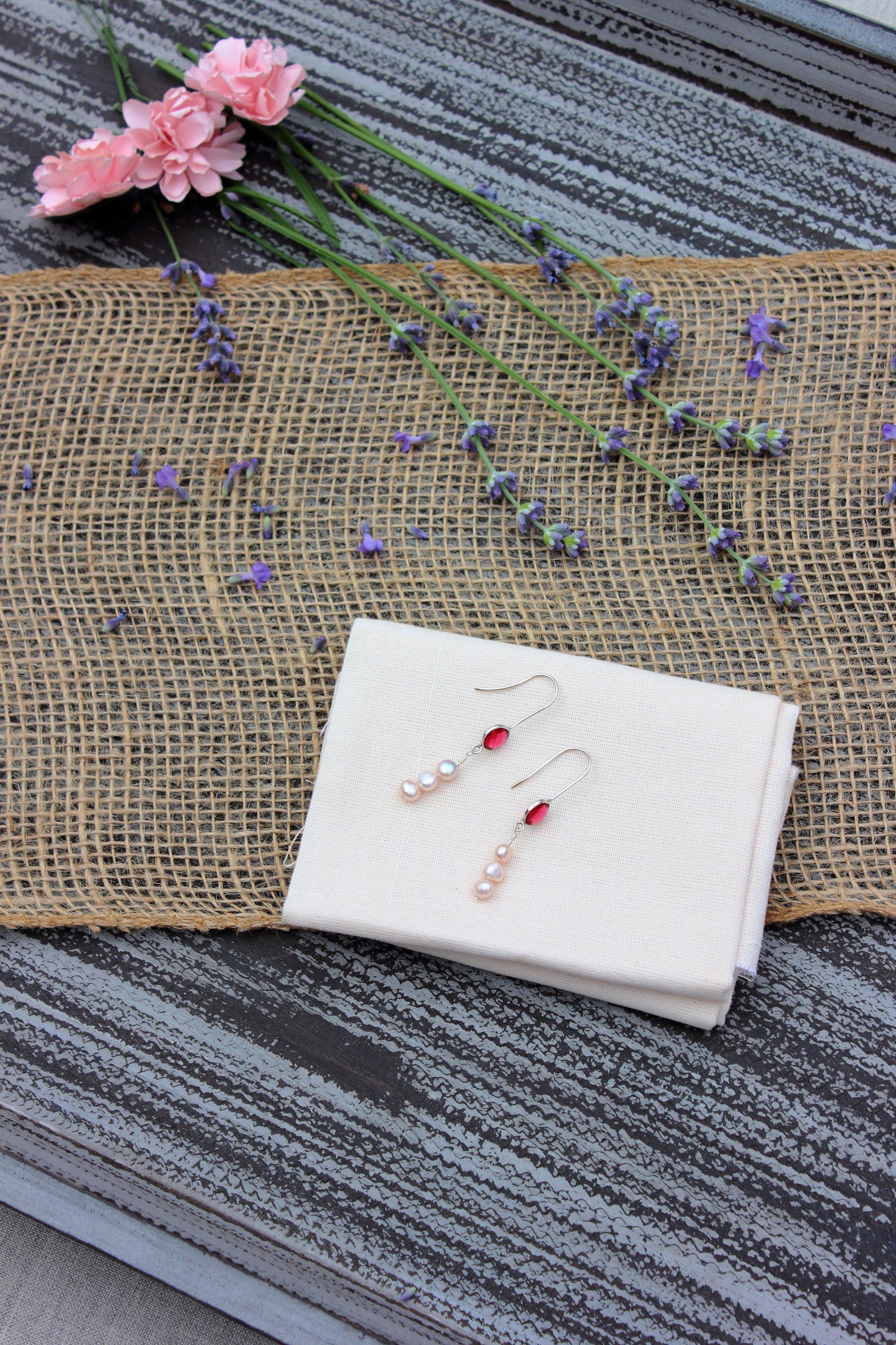 Pair of earrings on a white cloth with flowers in the background