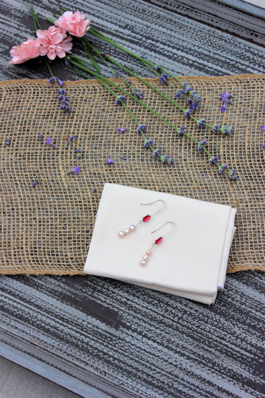 Pair of earrings on a white cloth with flowers in the background