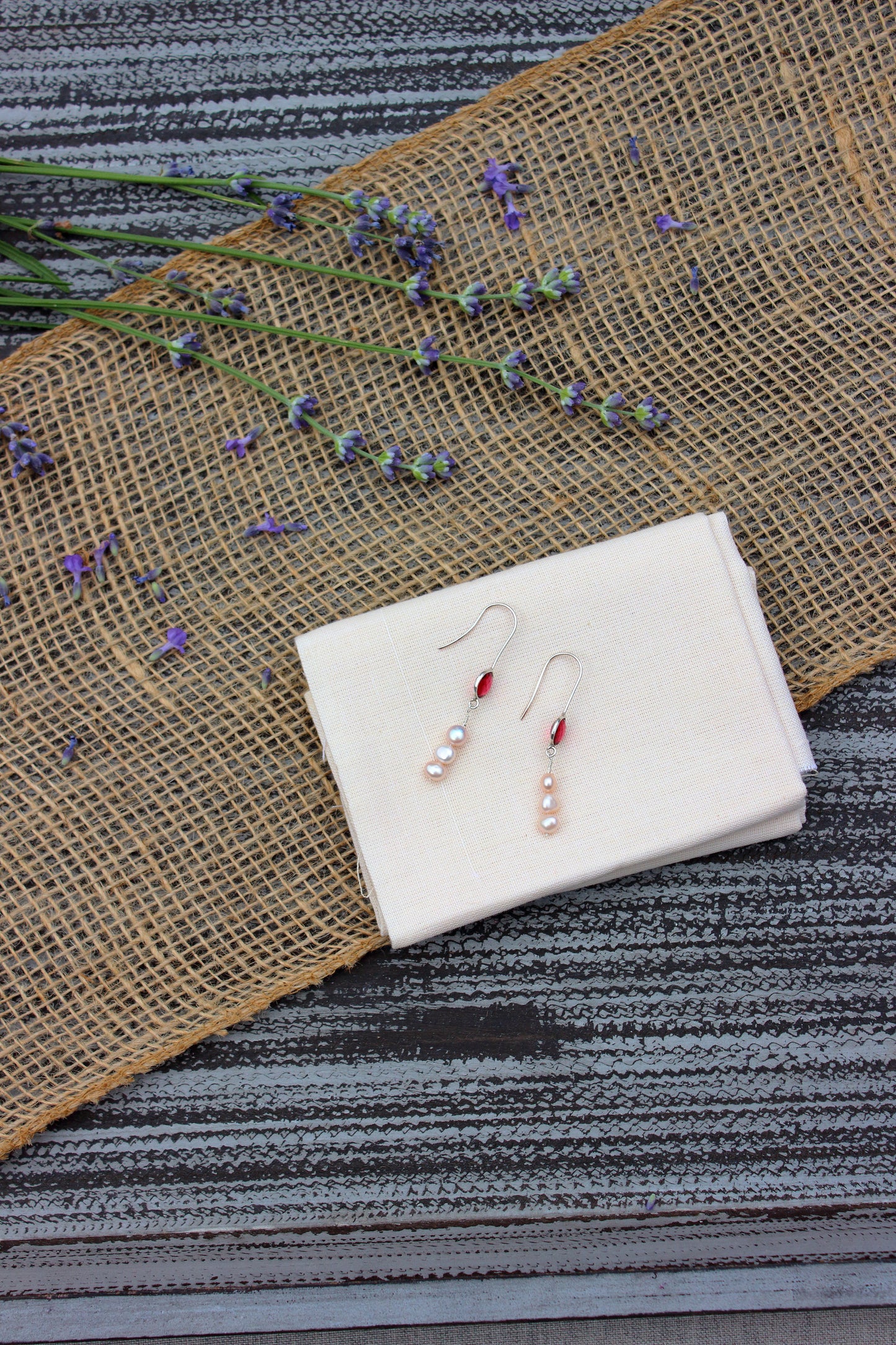 Pair of earrings with a beige fabric and lavender flowers on a striped surface