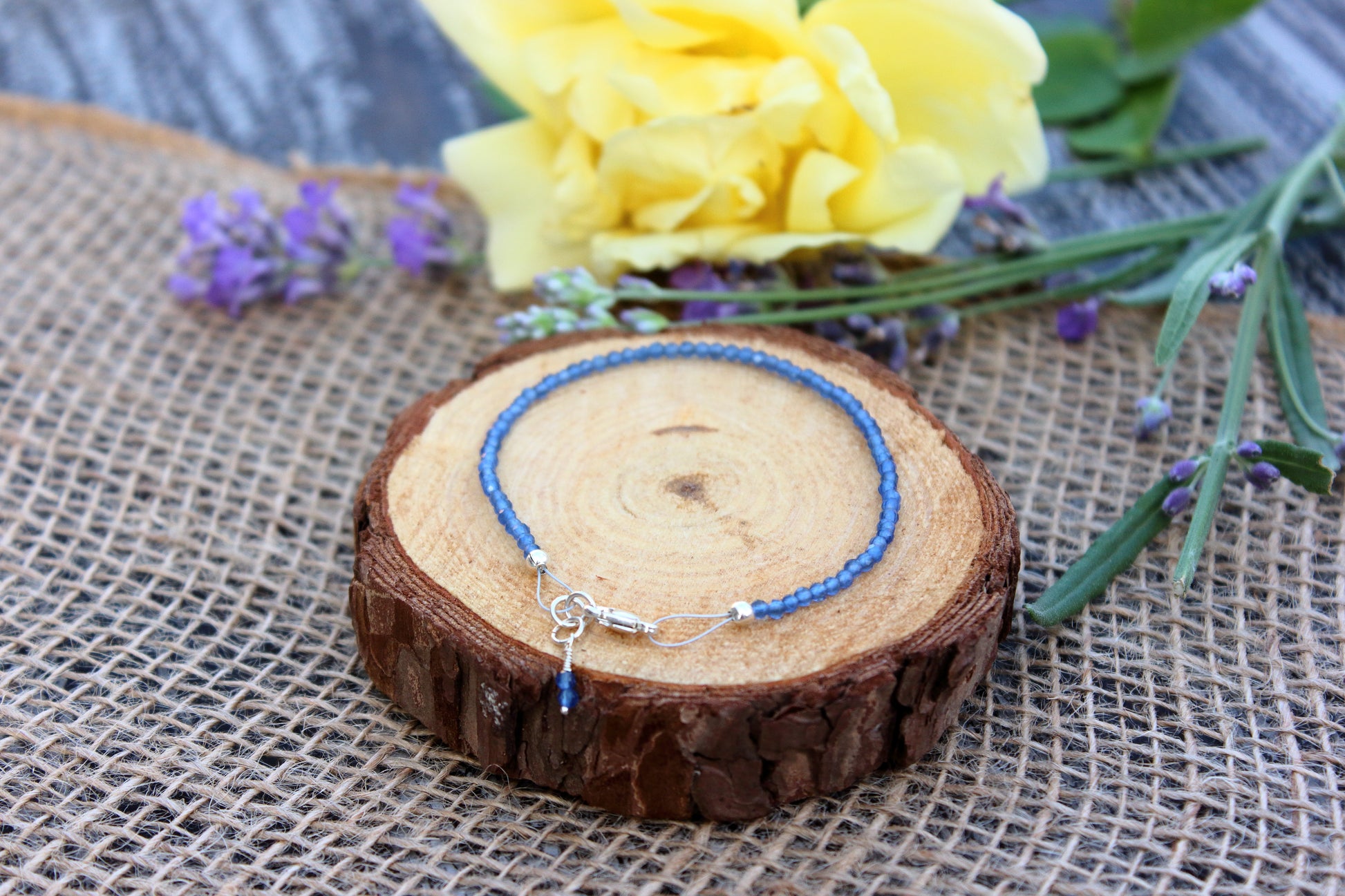 Blue beaded bracelet on a wooden slice with flowers in the background