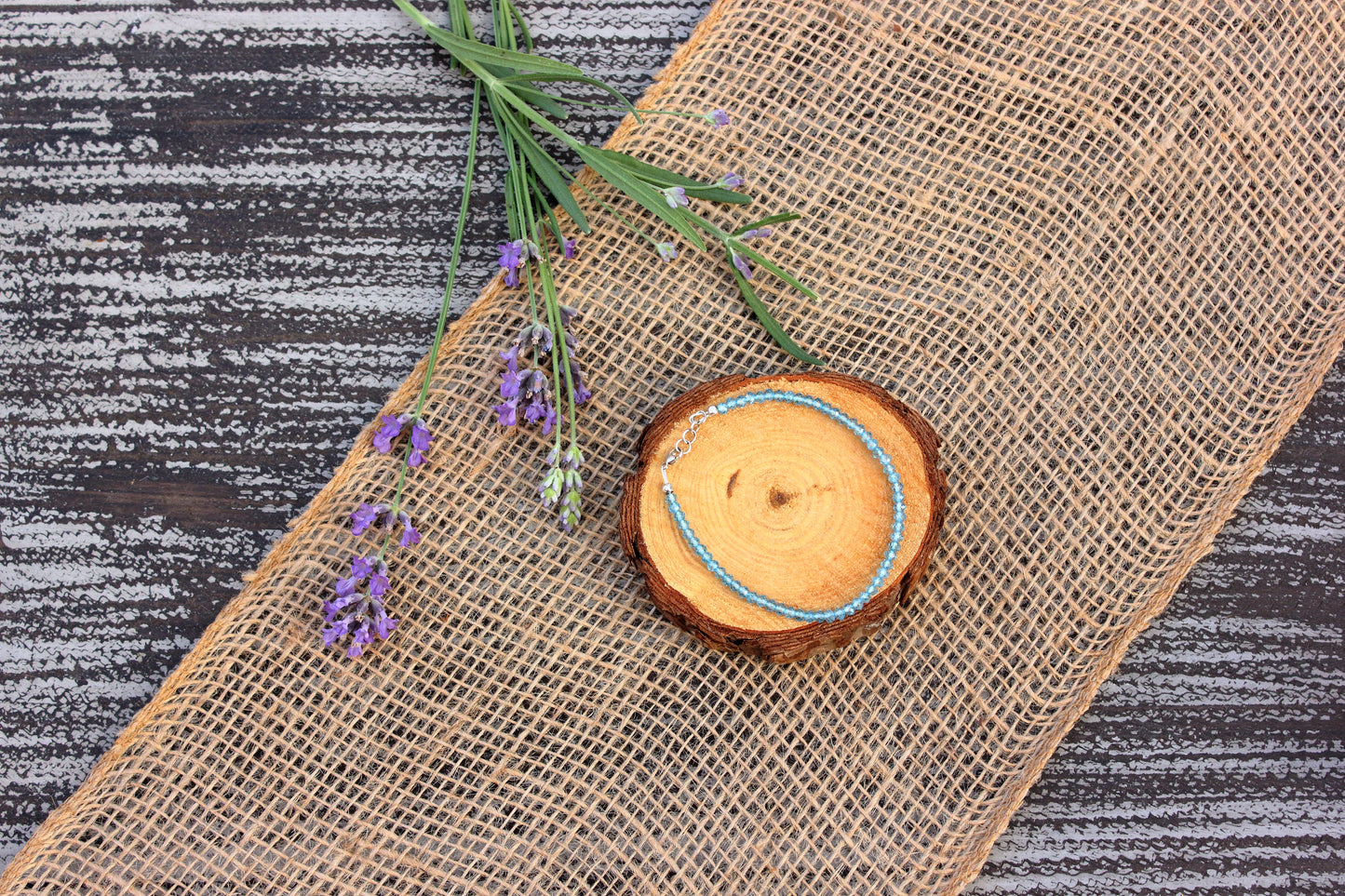 Wooden slice with a blue string on a textured surface with lavender flowers