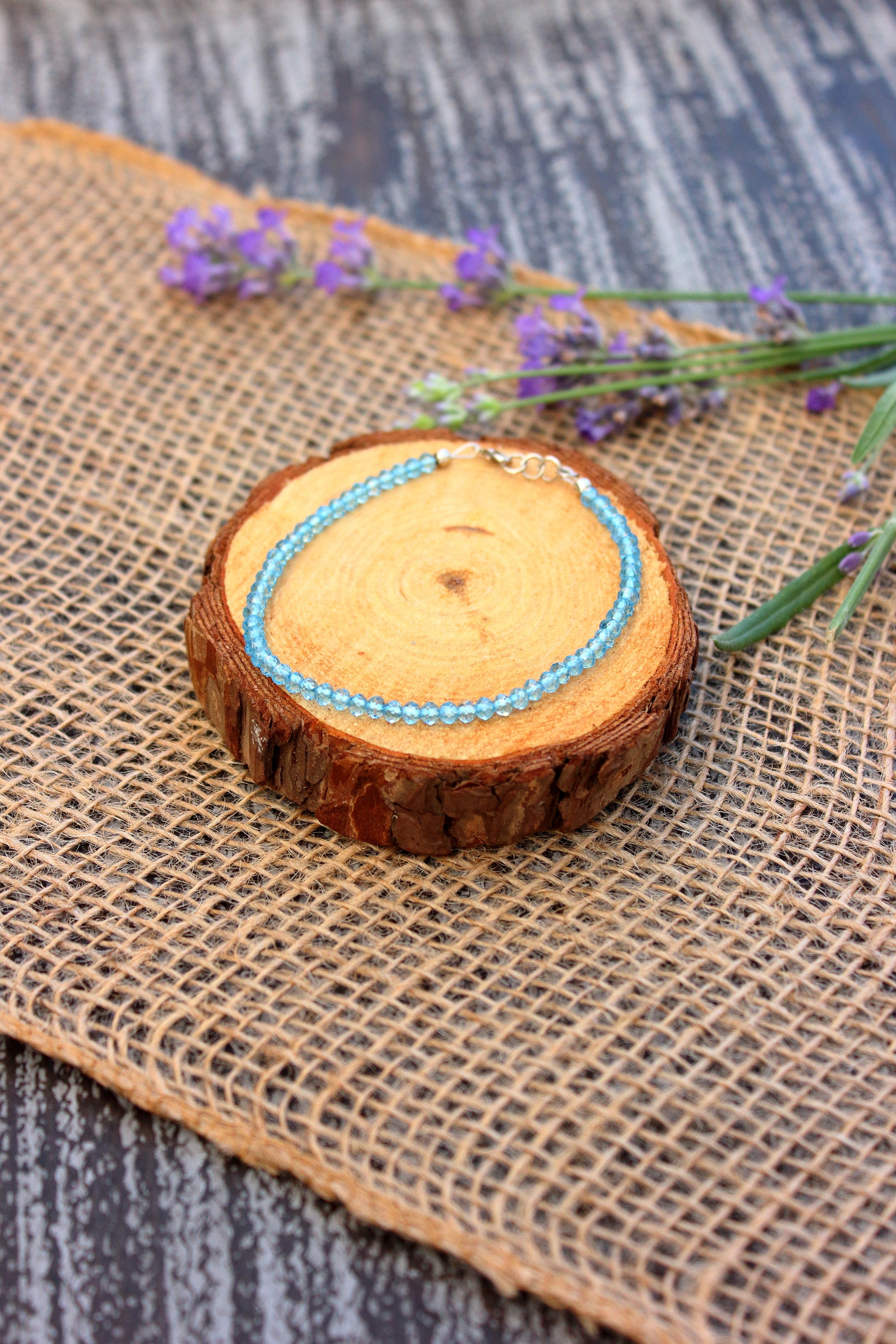Blue beaded bracelet on a wooden slice with lavender flowers on a textured surface