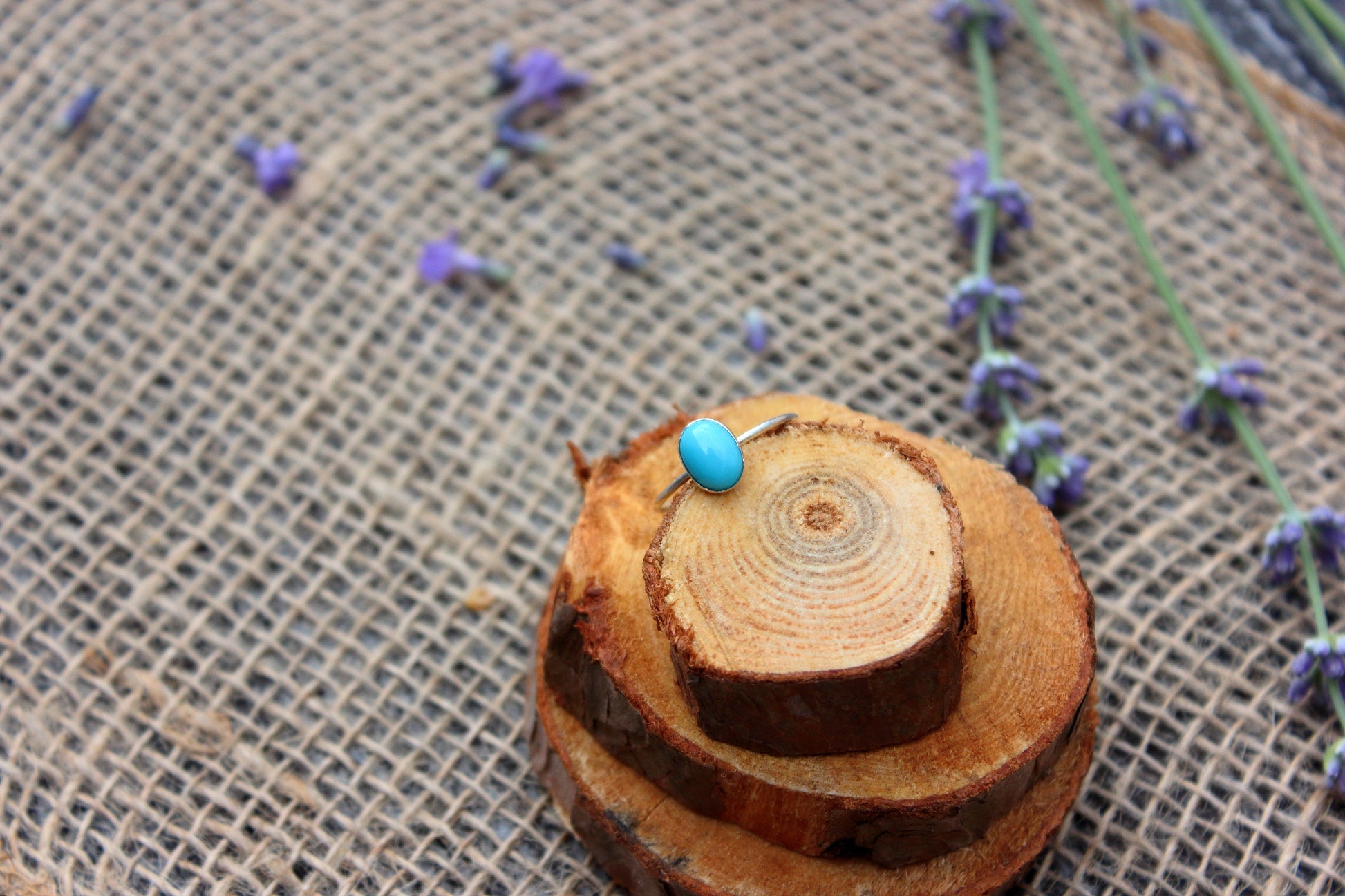Ring with a blue gemstone on a textured fabric background with lavender flowers.