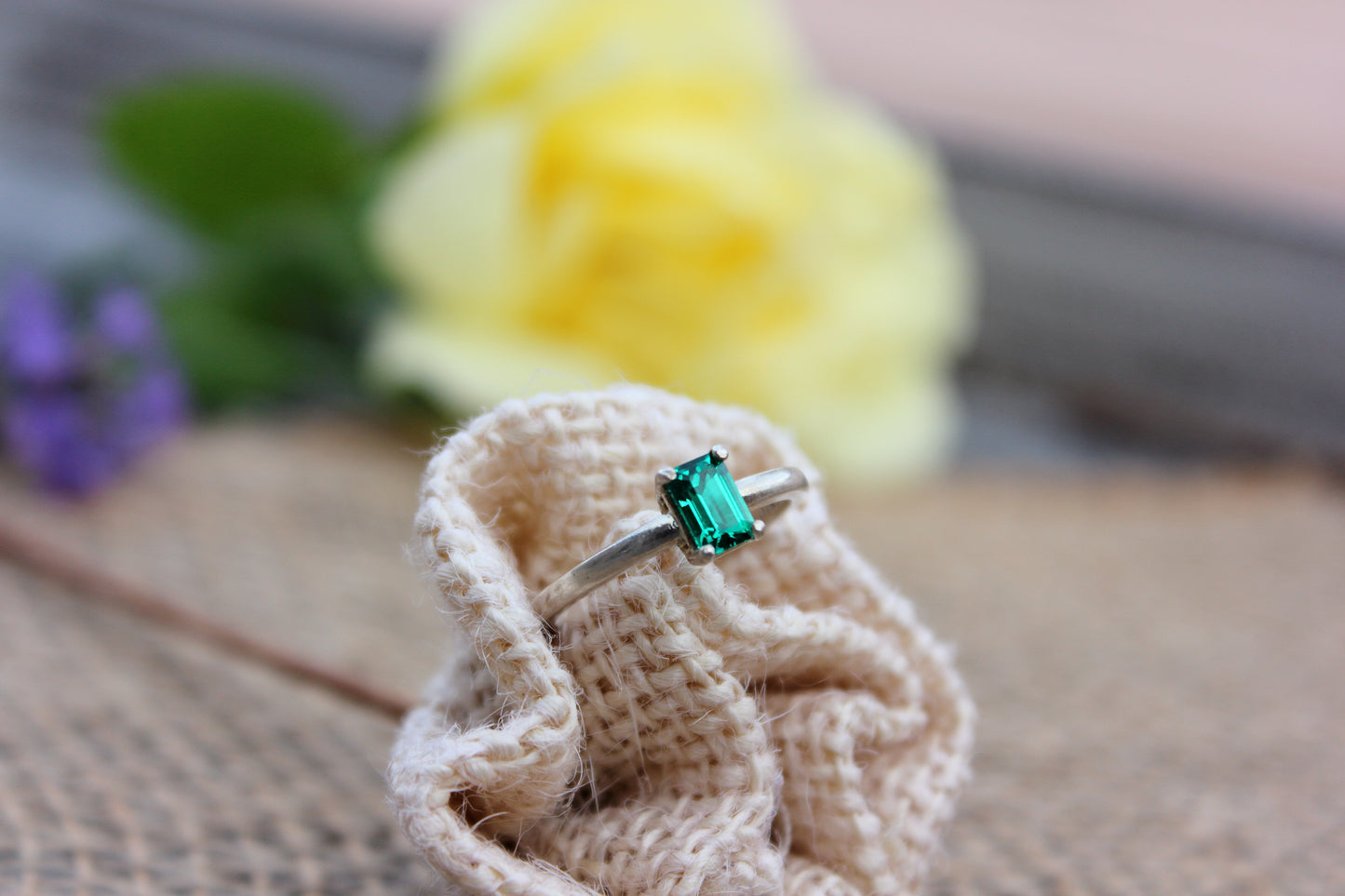 Ring with a green gemstone on a woven mat with flowers in the background