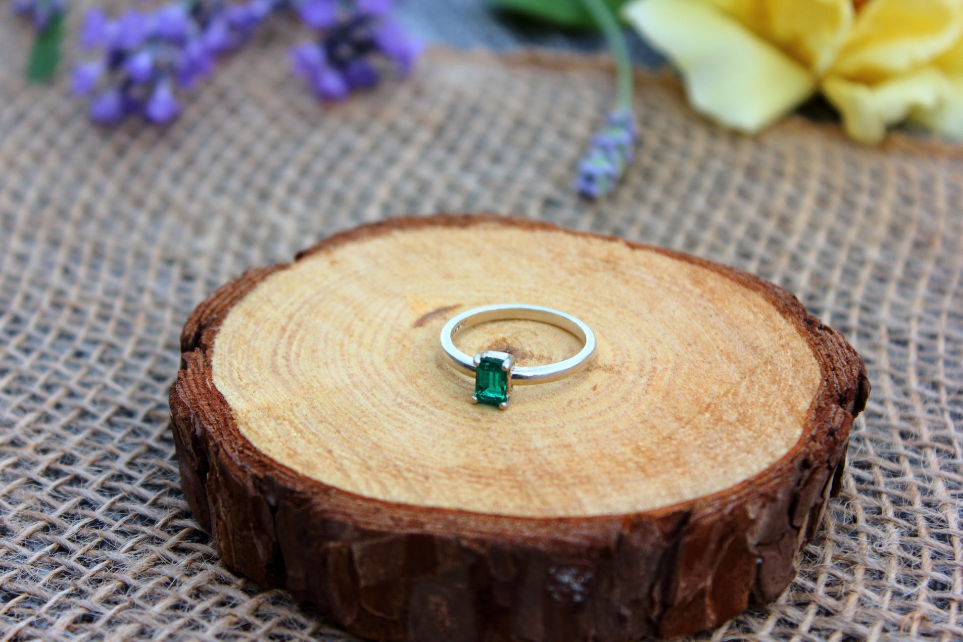 Silver ring with a green gemstone on a wooden slice with flowers in the background