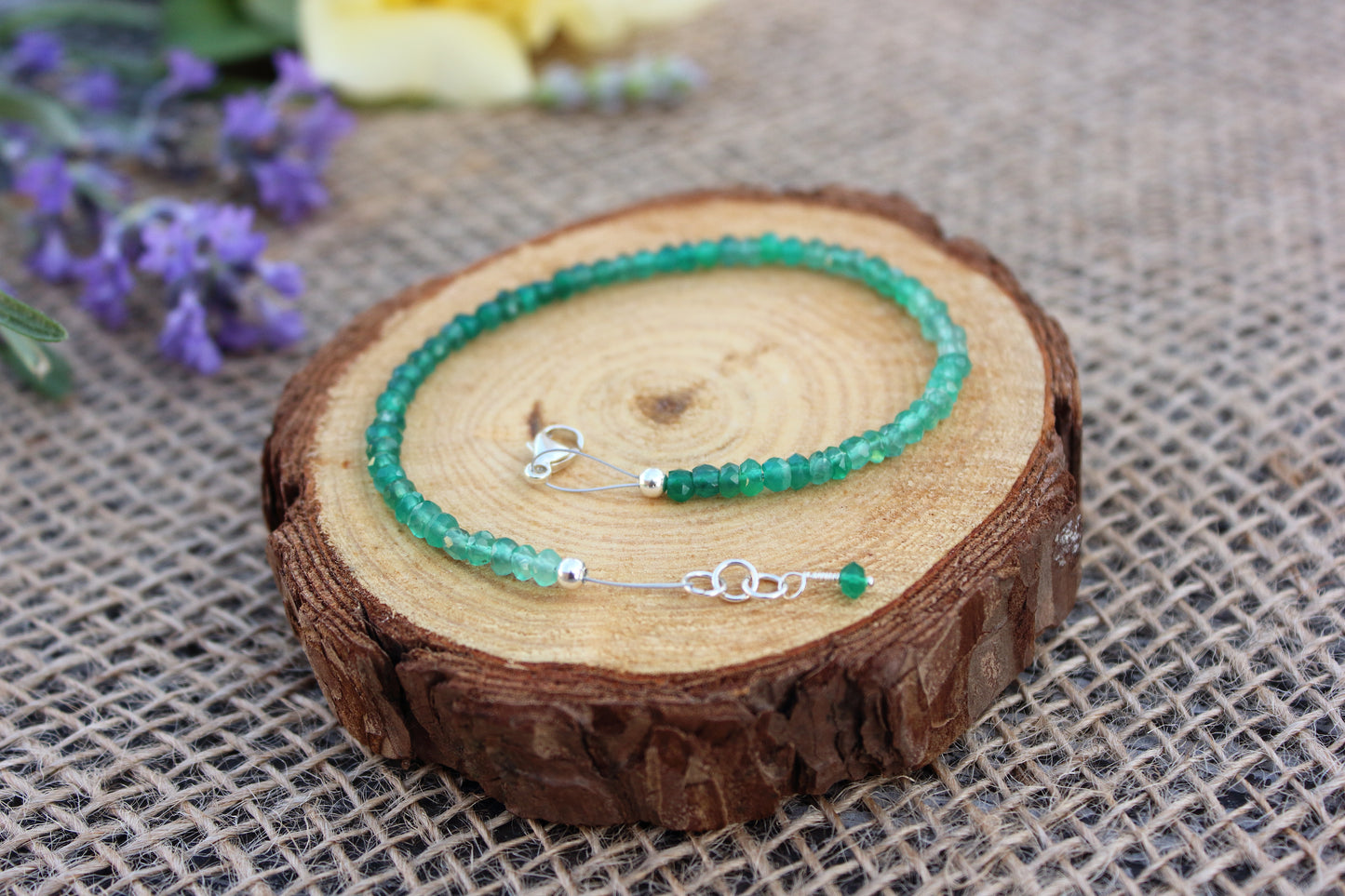 Green beaded bracelet on a wooden slice with flowers in the background