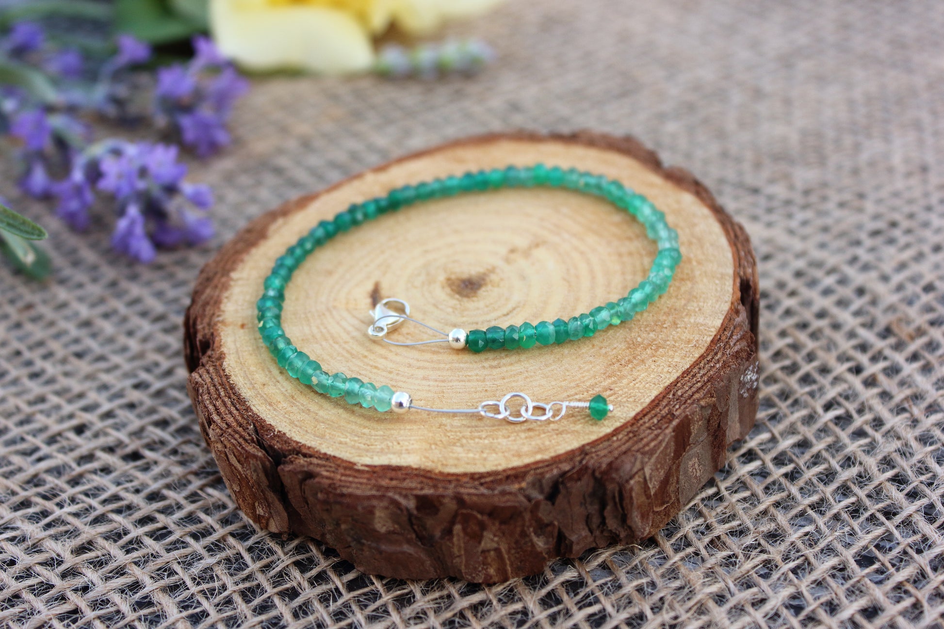 Green beaded bracelet on a wooden slice with flowers in the background