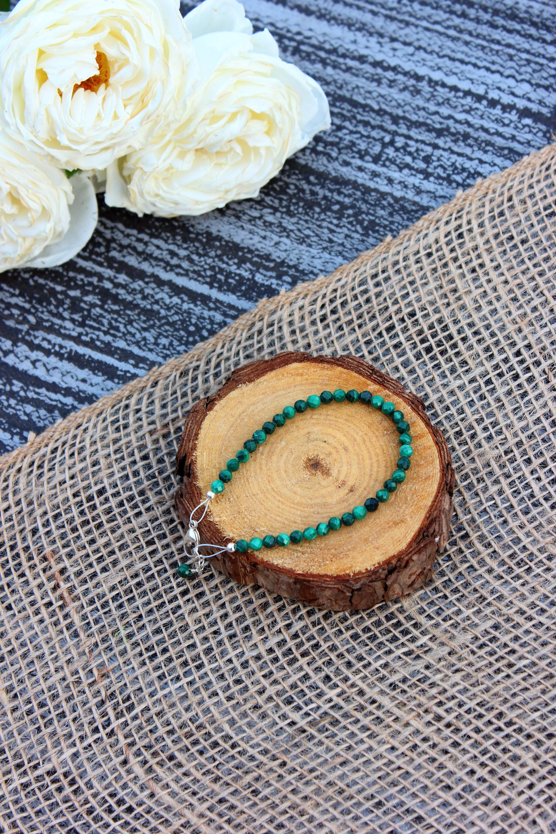 Green beaded necklace on a wooden slice with white flowers in the background