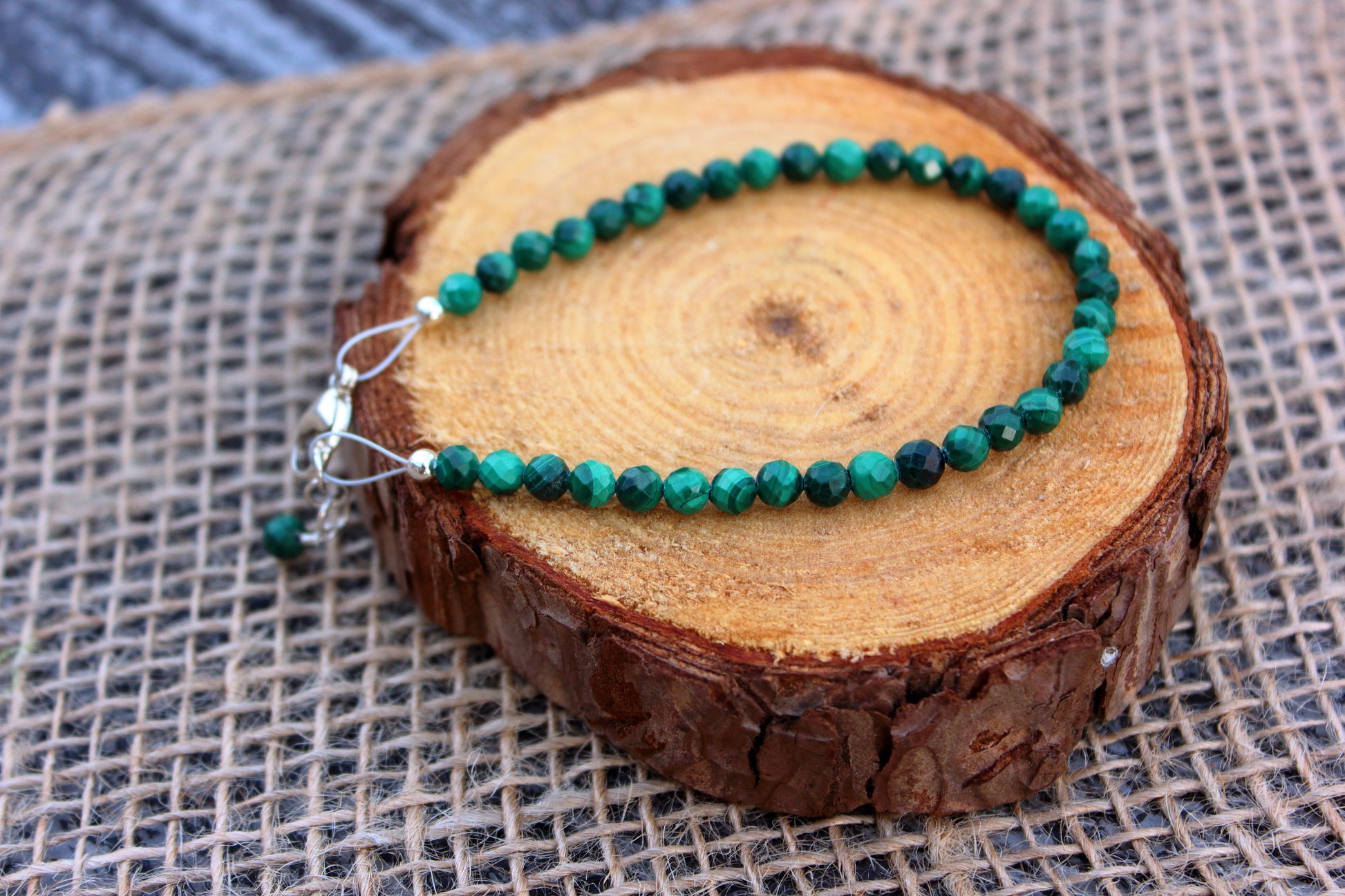 Green beaded bracelet on a wooden log with a textured fabric background