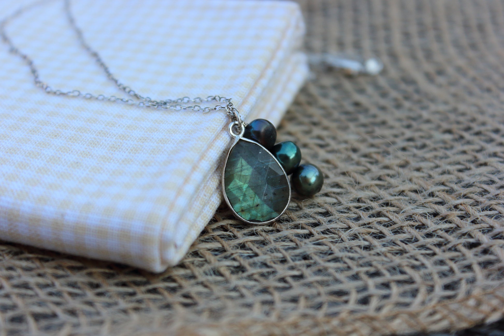 Necklace with green teardrop pendant and pearls on a textured surface