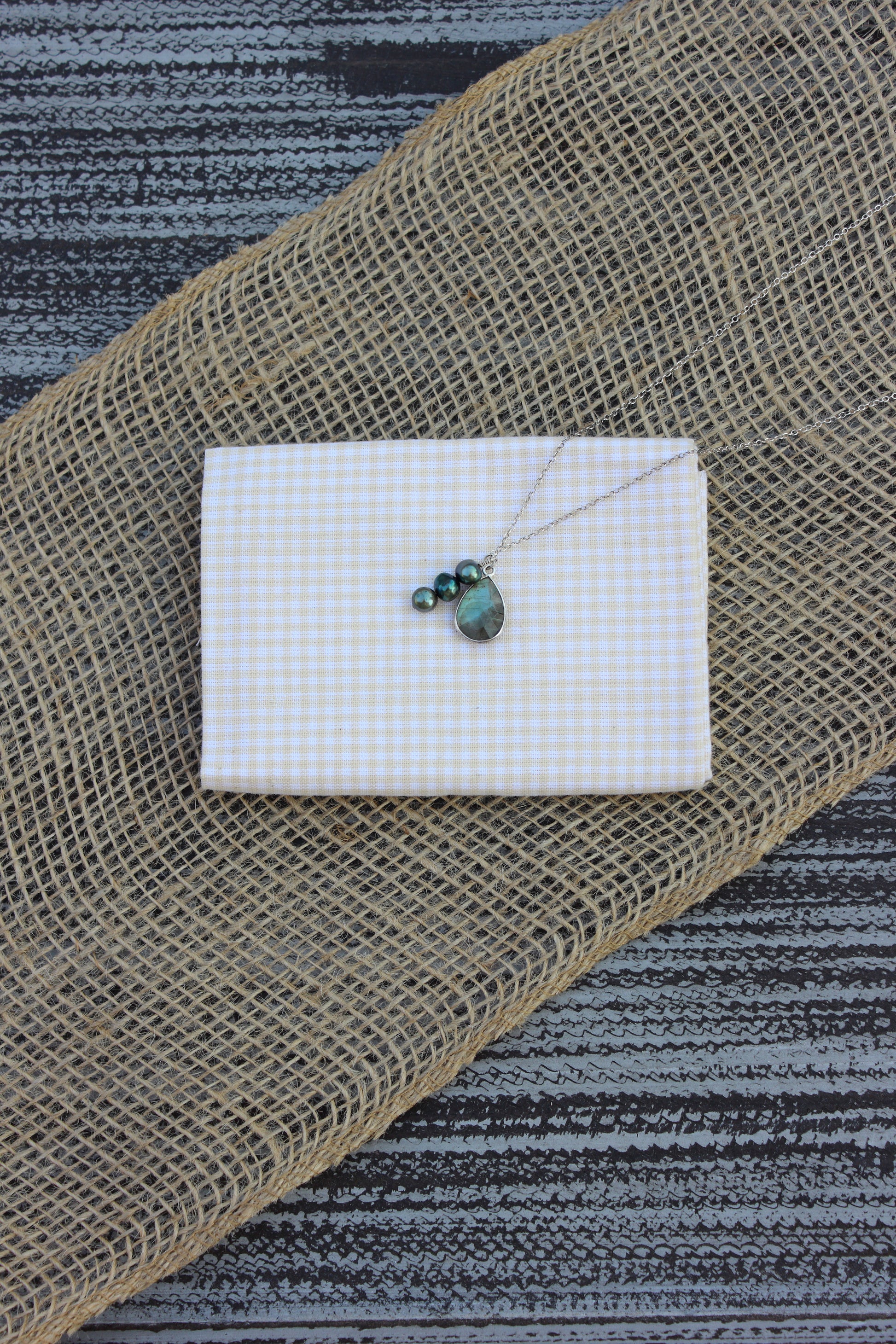 Necklace with a pendant on a white card, placed on a textured surface.