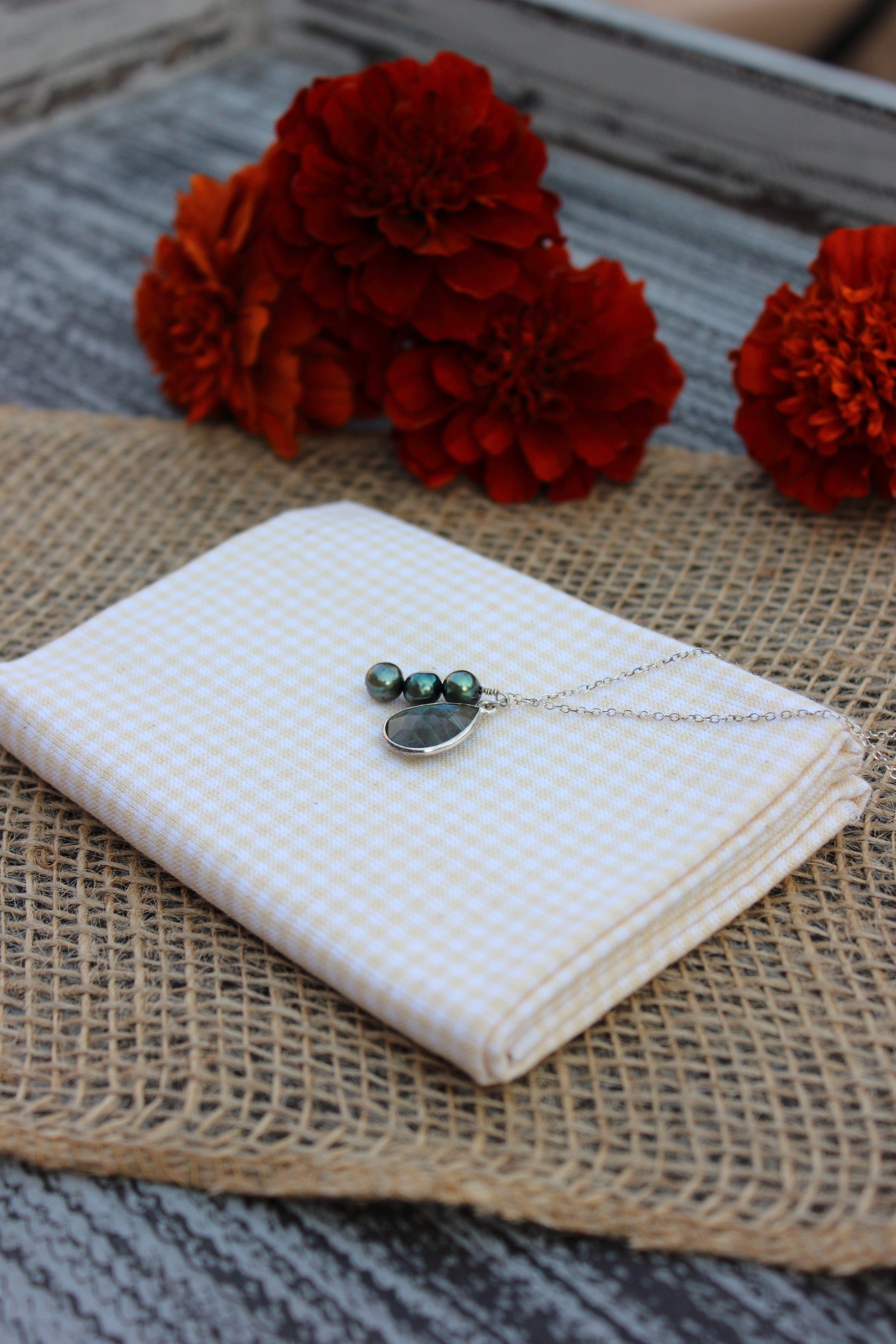 Necklace with pear shaped pendant on a white fabric with red flowers in the background