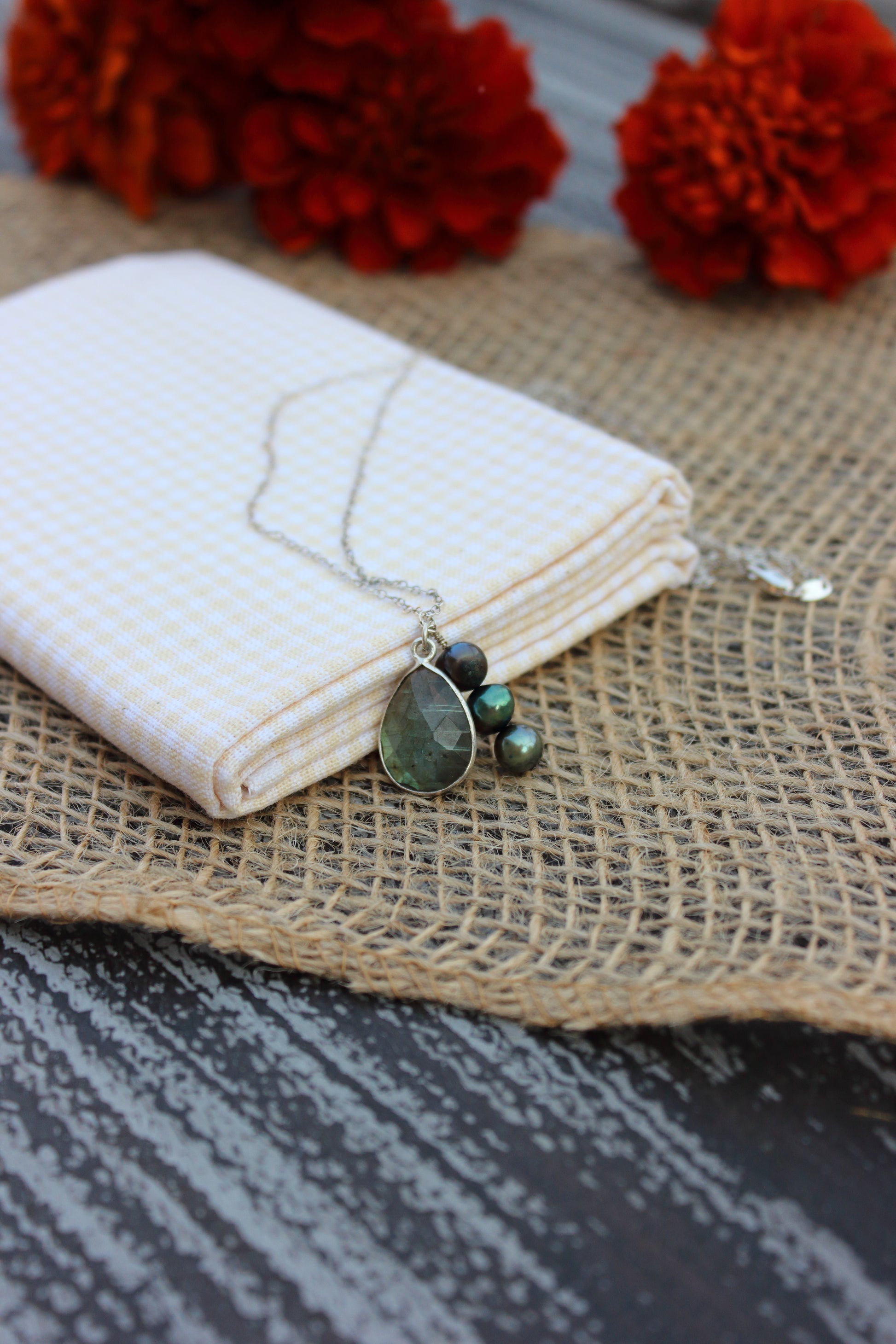 Necklace with green teardrop pendants on a white fabric with red flowers in the background