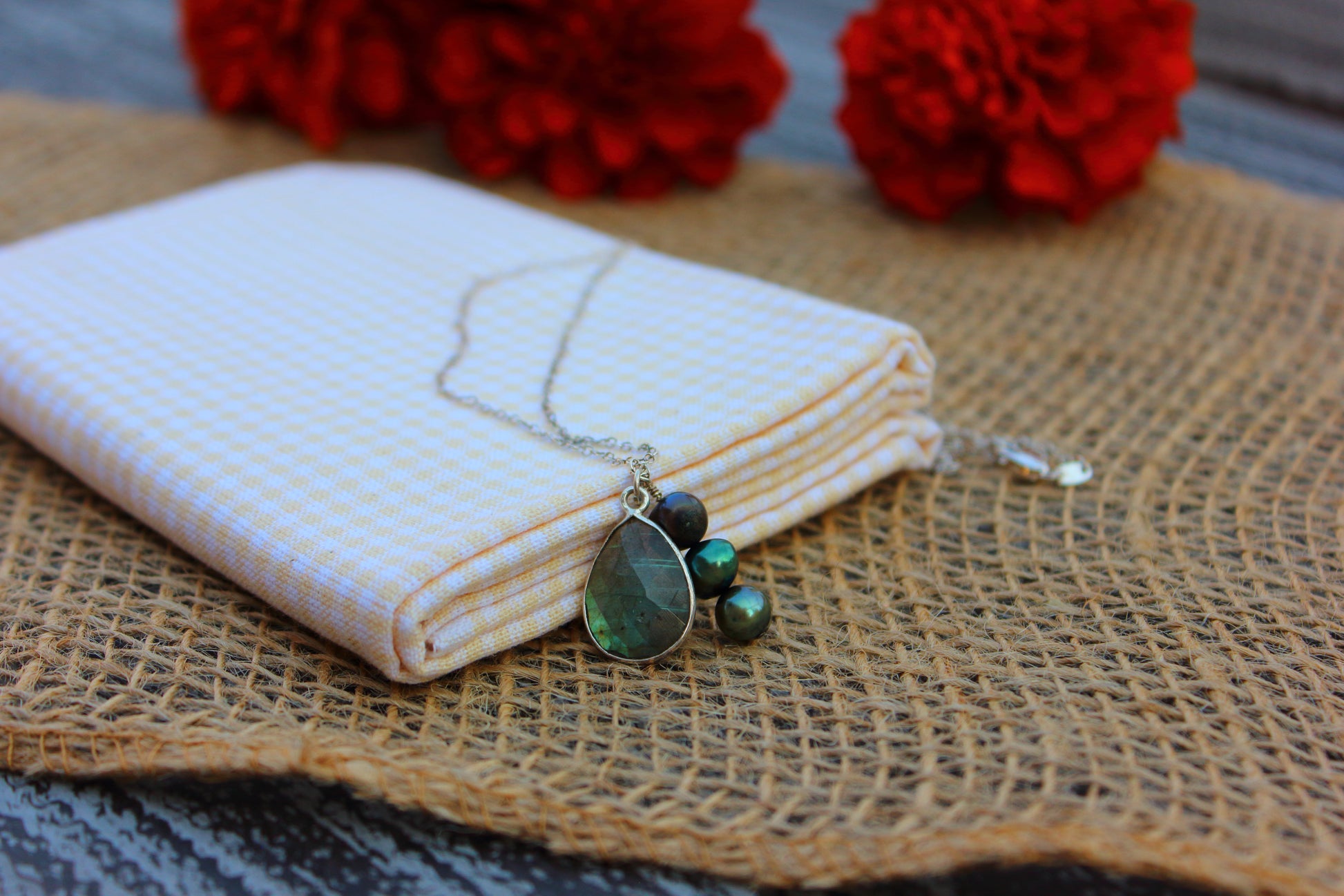 Necklace with green beads on a white fabric and burlap surface with red flowers in the background