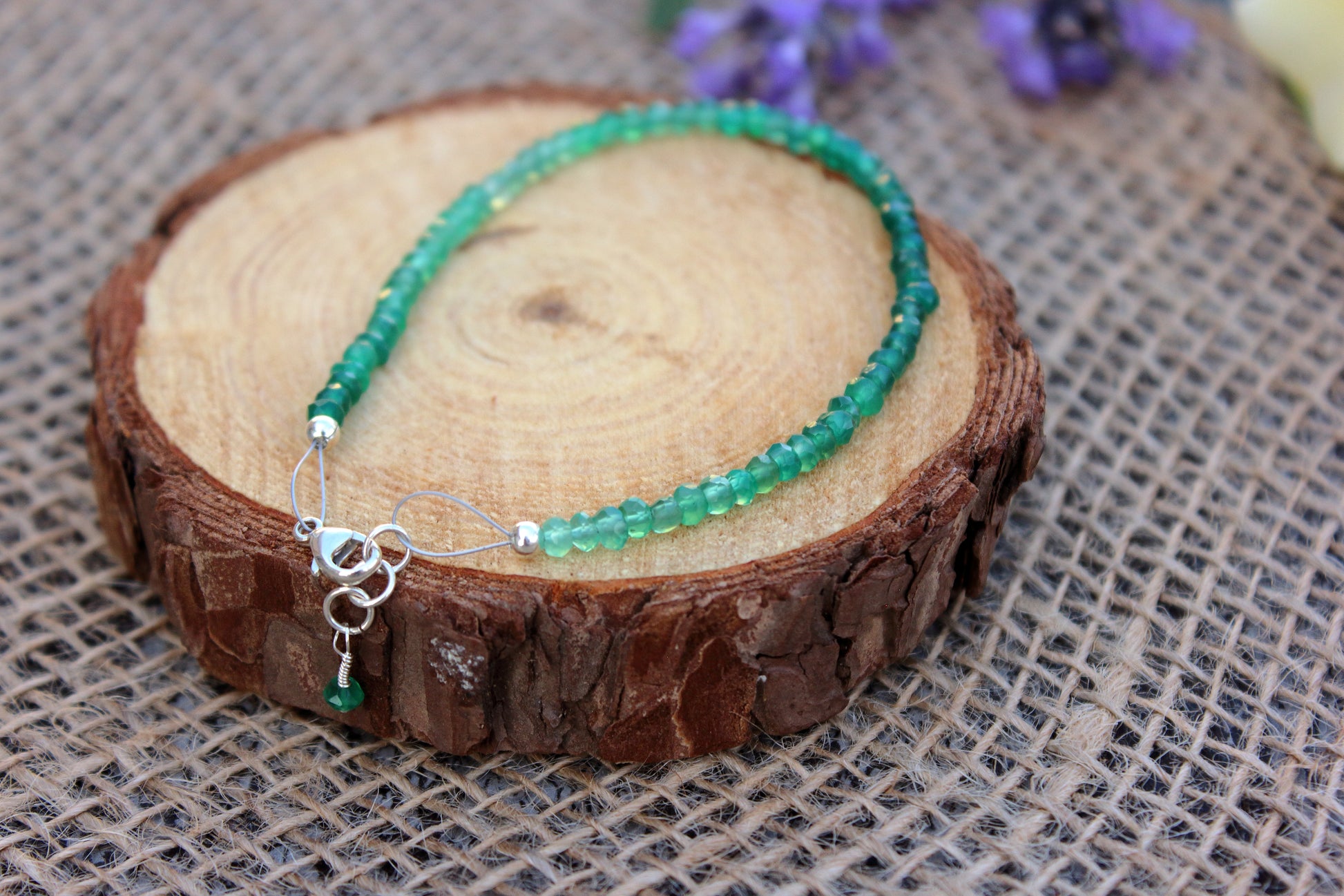Green beaded necklace on a wooden block with a textured fabric background