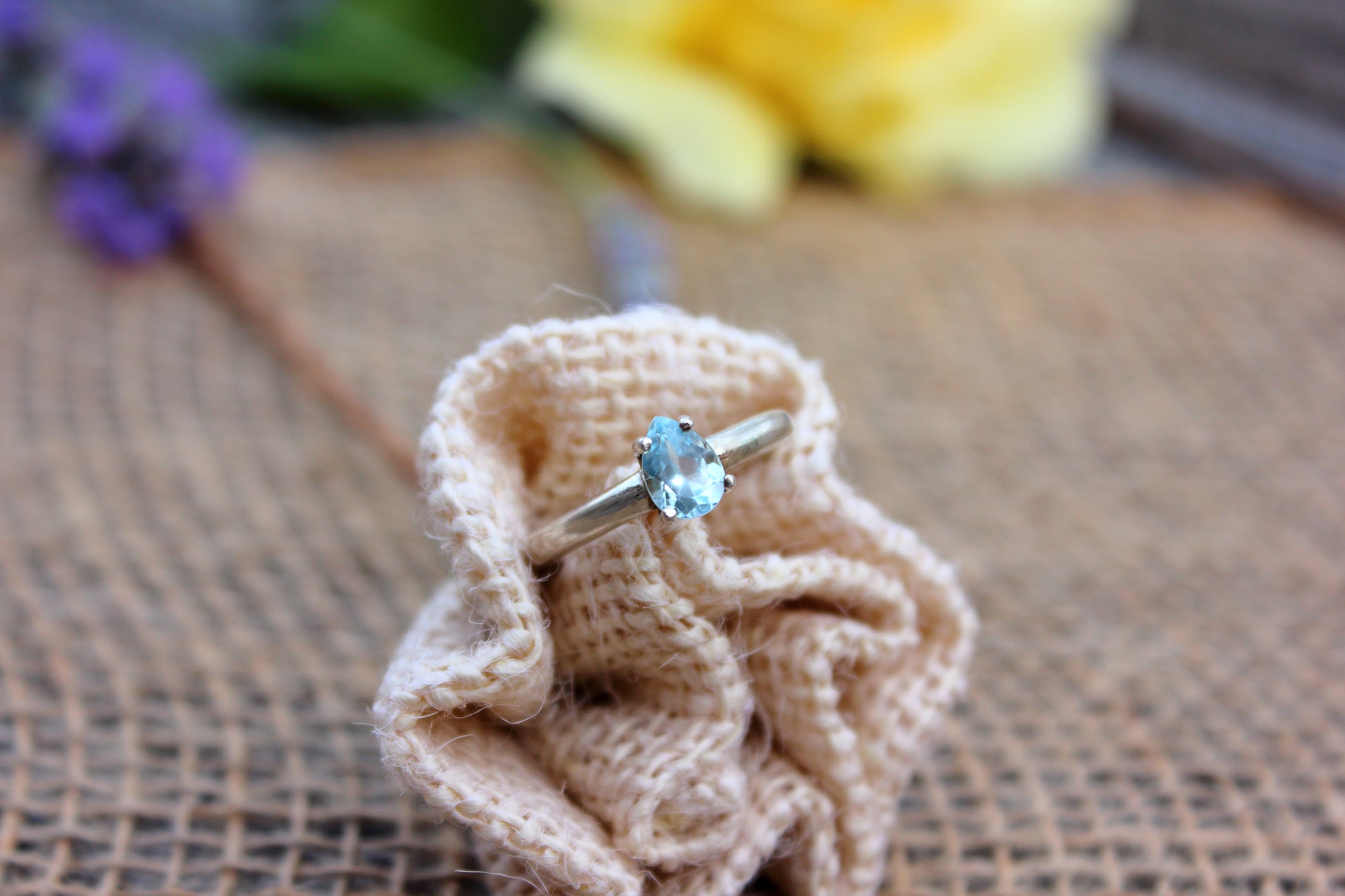 Silver ring with a blue gemstone on a beige knitted fabric against a blurred natural background
