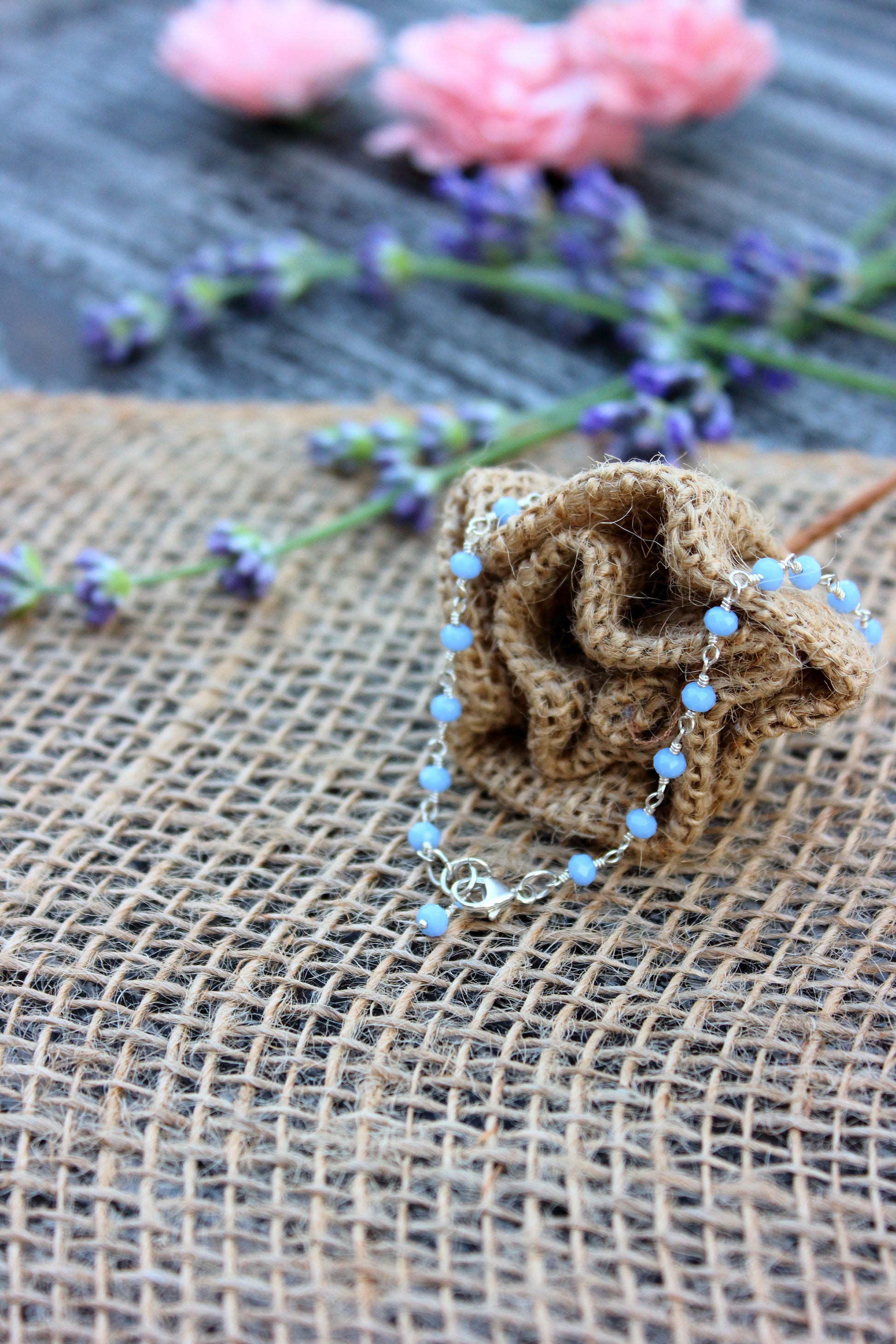 Bracelet with blue beads on a burlap surface with flowers in the background