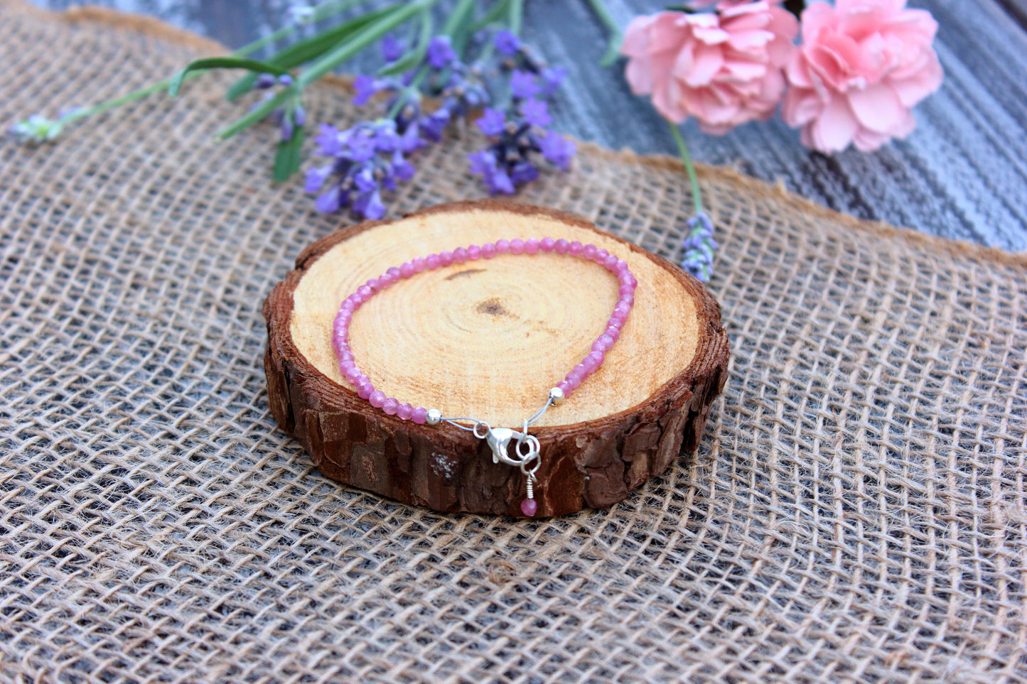 Pink beaded bracelet on a wooden slice with flowers in the background