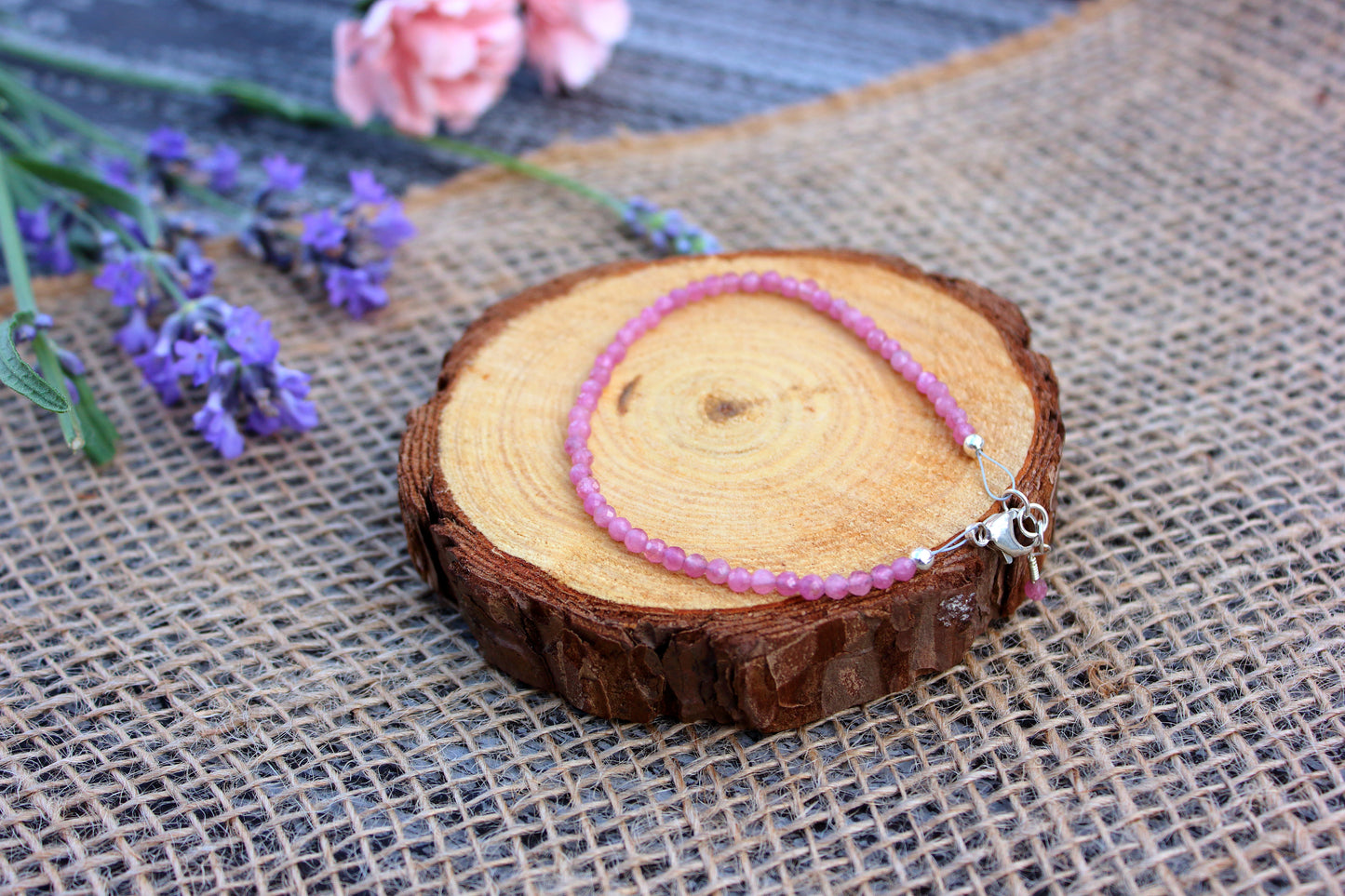 Pink beaded bracelet on a wooden slice with flowers in the background
