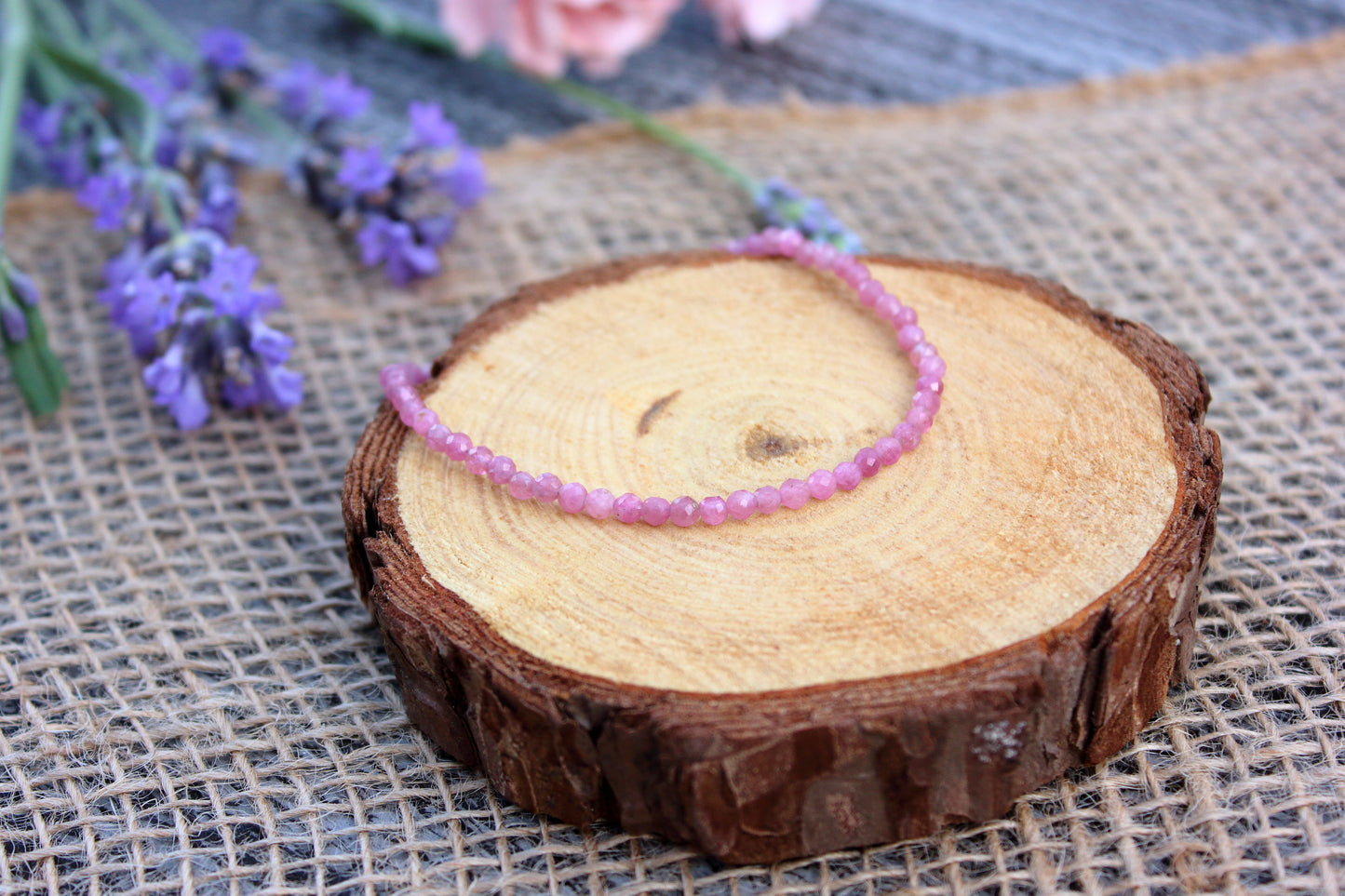 Pink beaded bracelet on a wooden slice with lavender flowers in the background