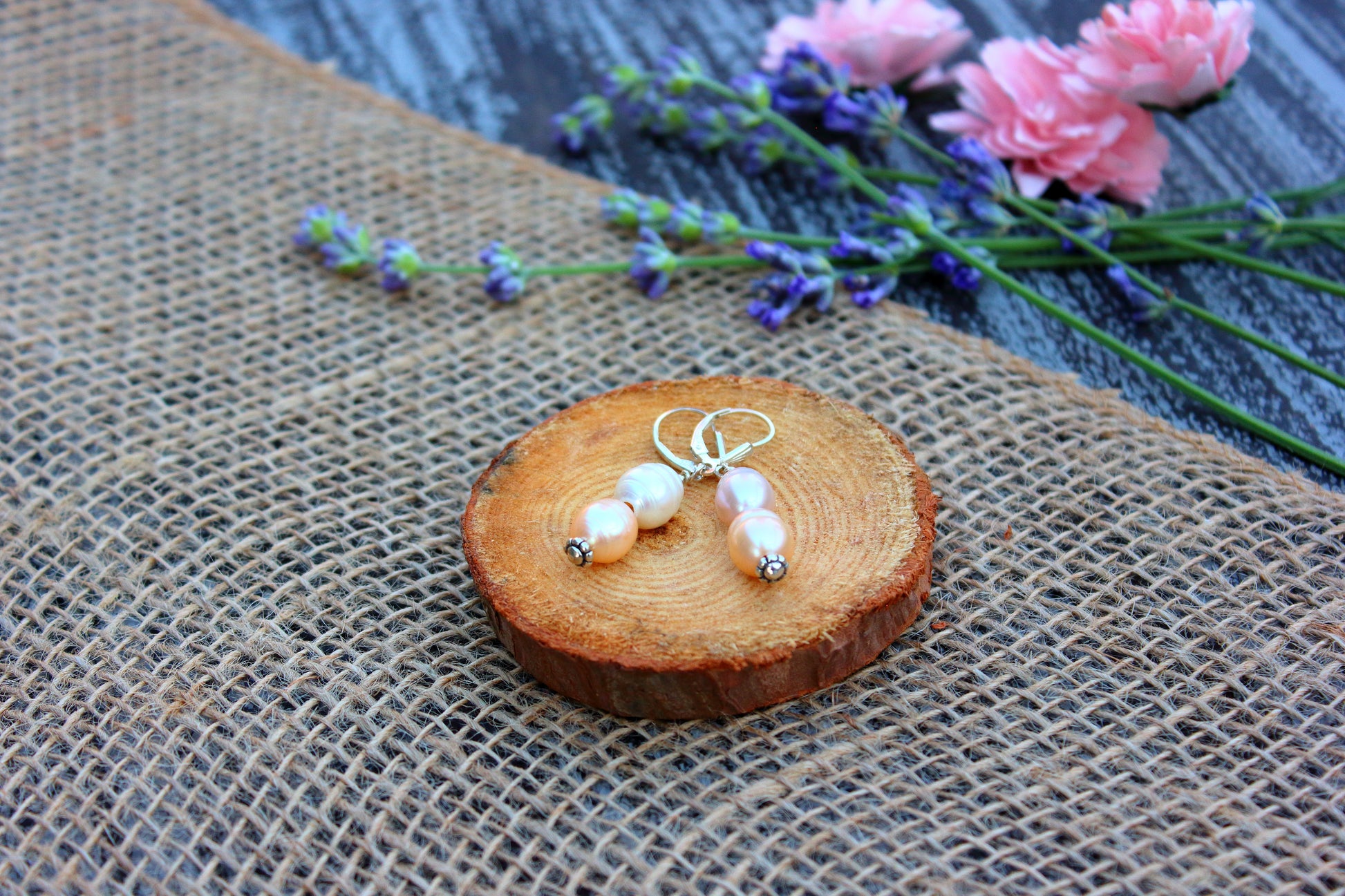 Pearl earrings on a wooden slice with flowers in the background