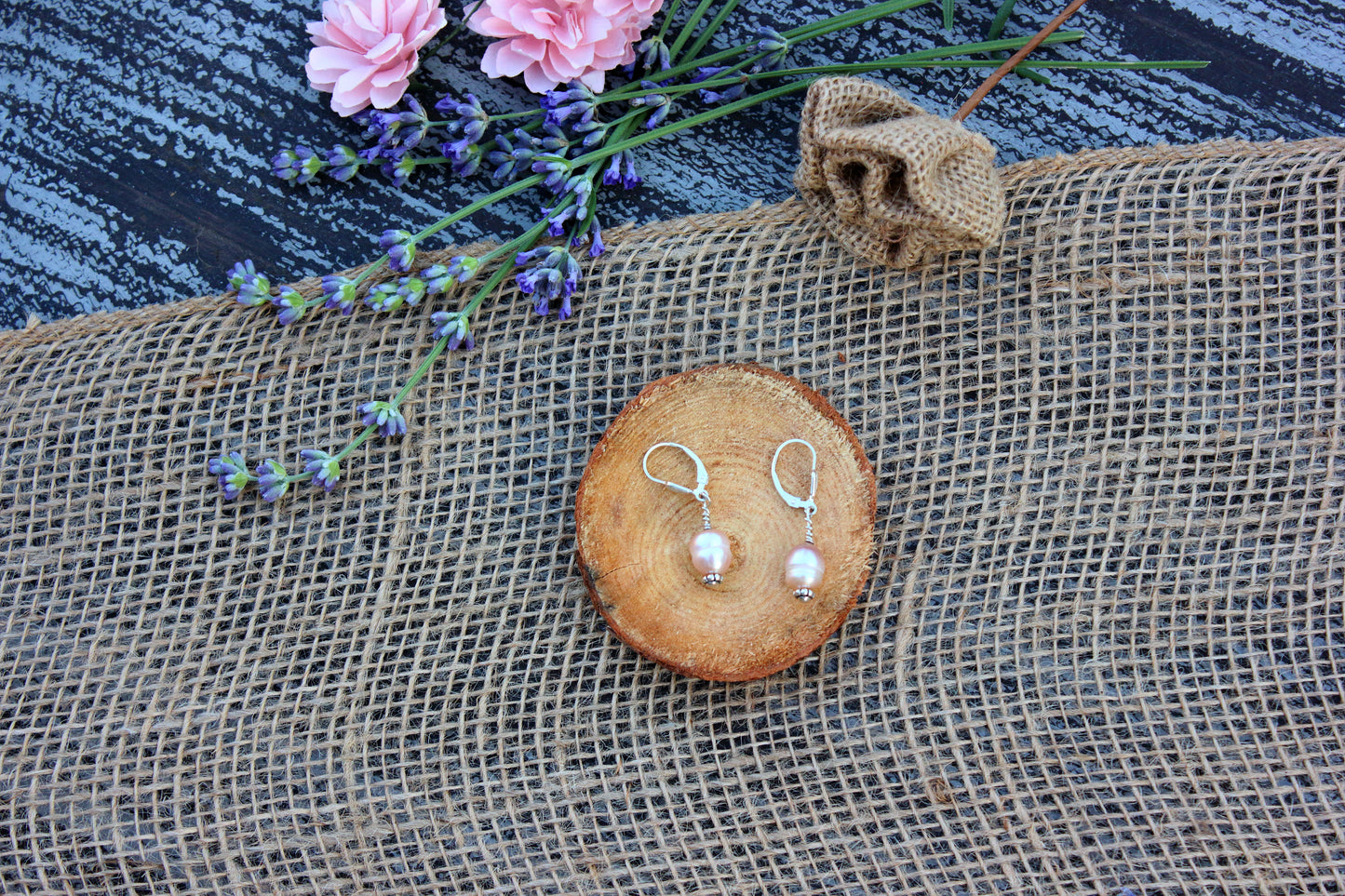 Silver earrings on a wooden coaster with flowers in the background