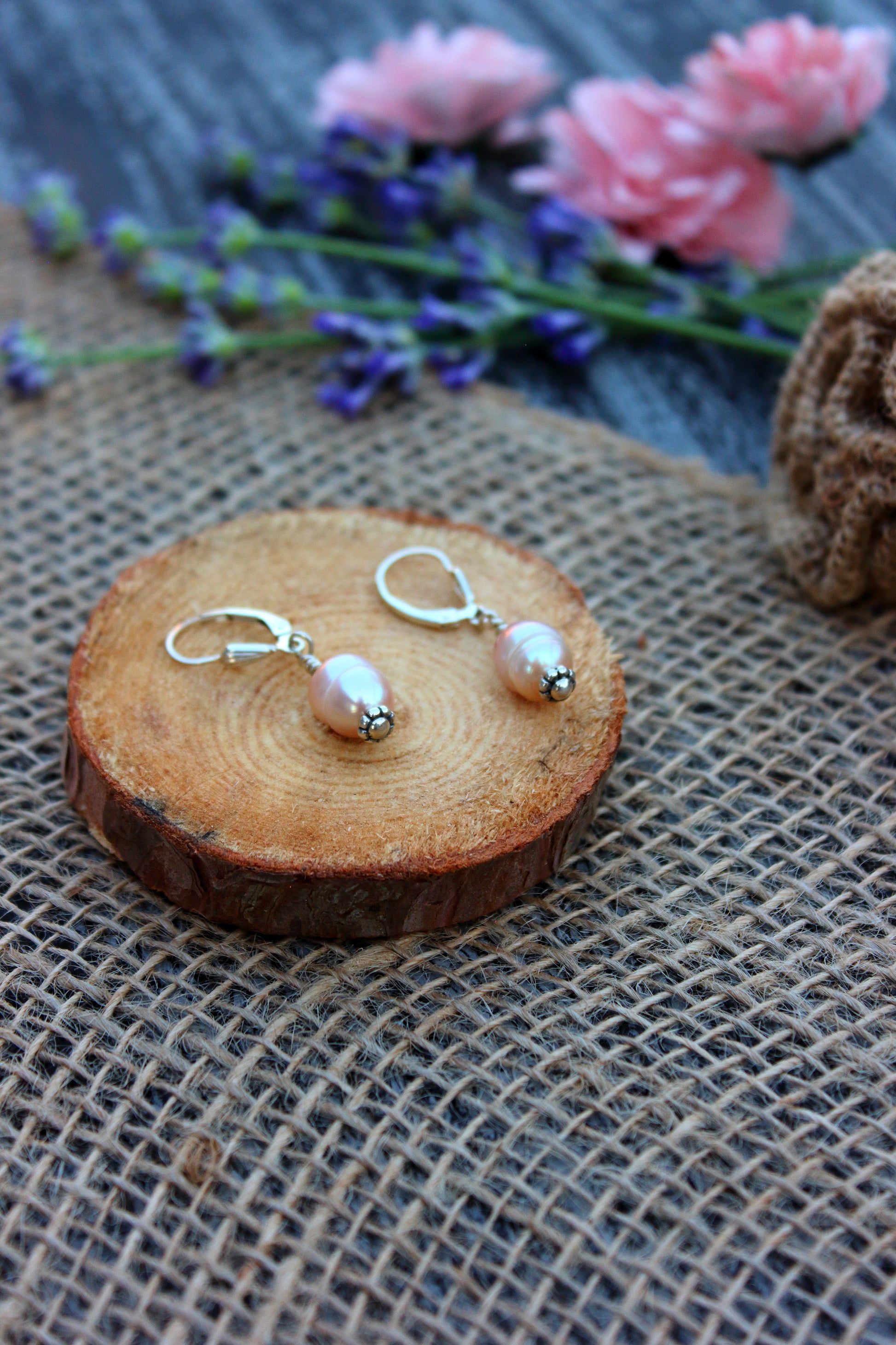 Pair of pearl earrings on a wooden slice with flowers in the background