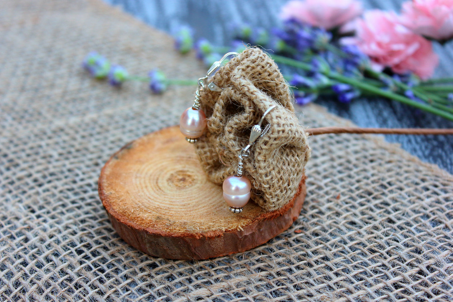 Pair of earrings with pink beads on a wooden surface with flowers in the background