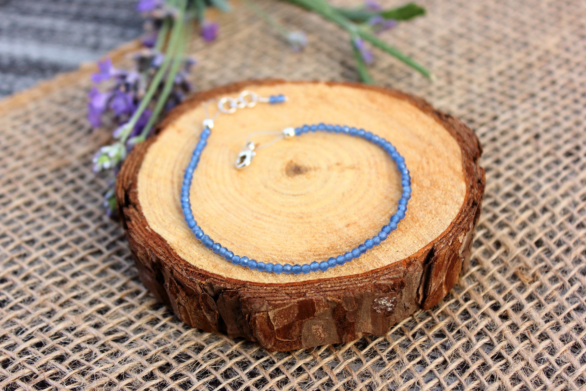 Blue beaded necklace on a wooden slice with lavender flowers in the background