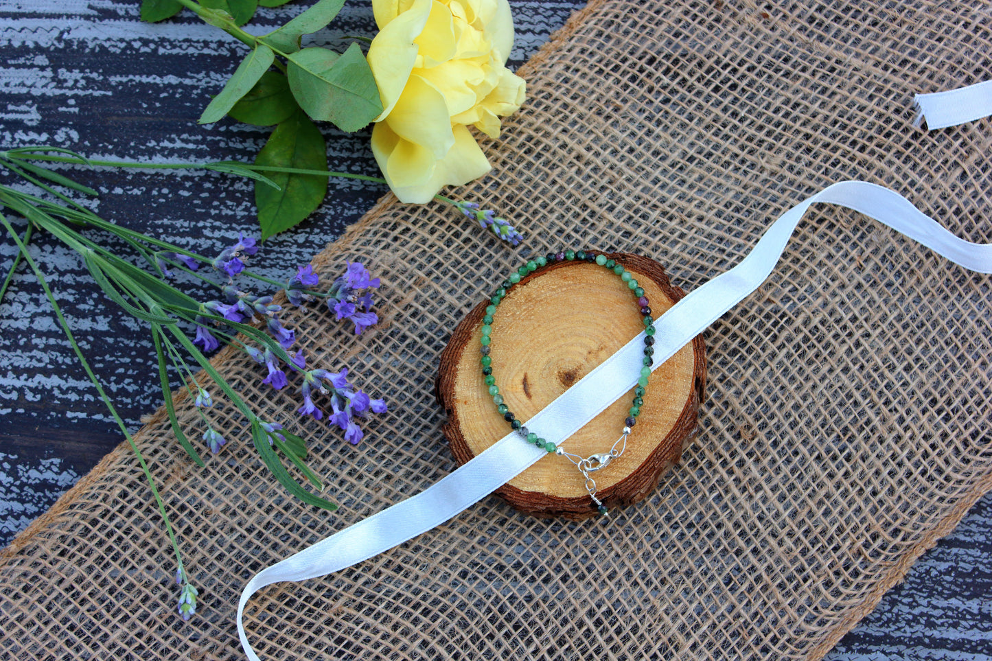 Beaded necklace, ribbon, and flowers on a textured surface