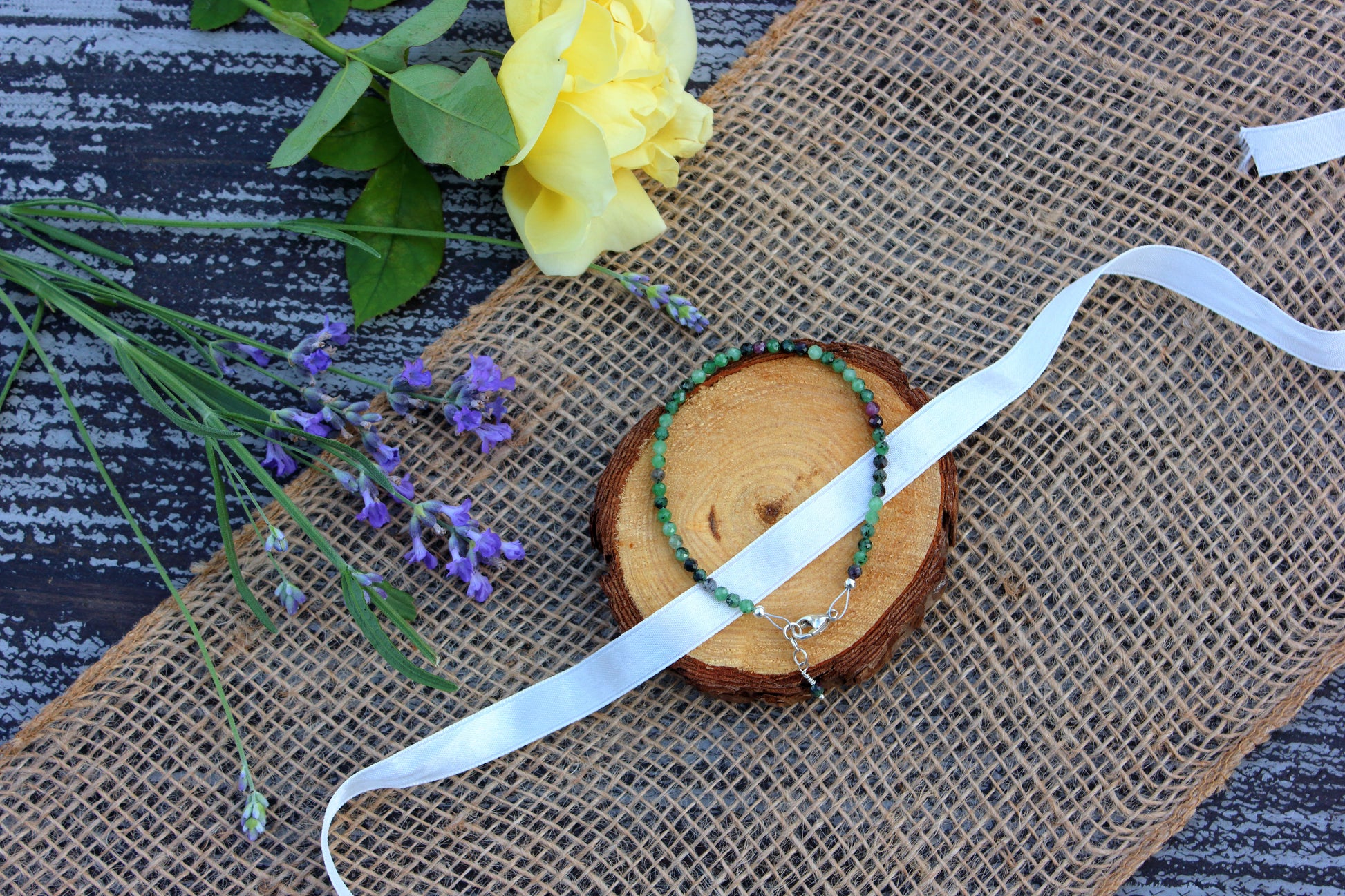 Beaded necklace, ribbon, and flowers on a textured surface