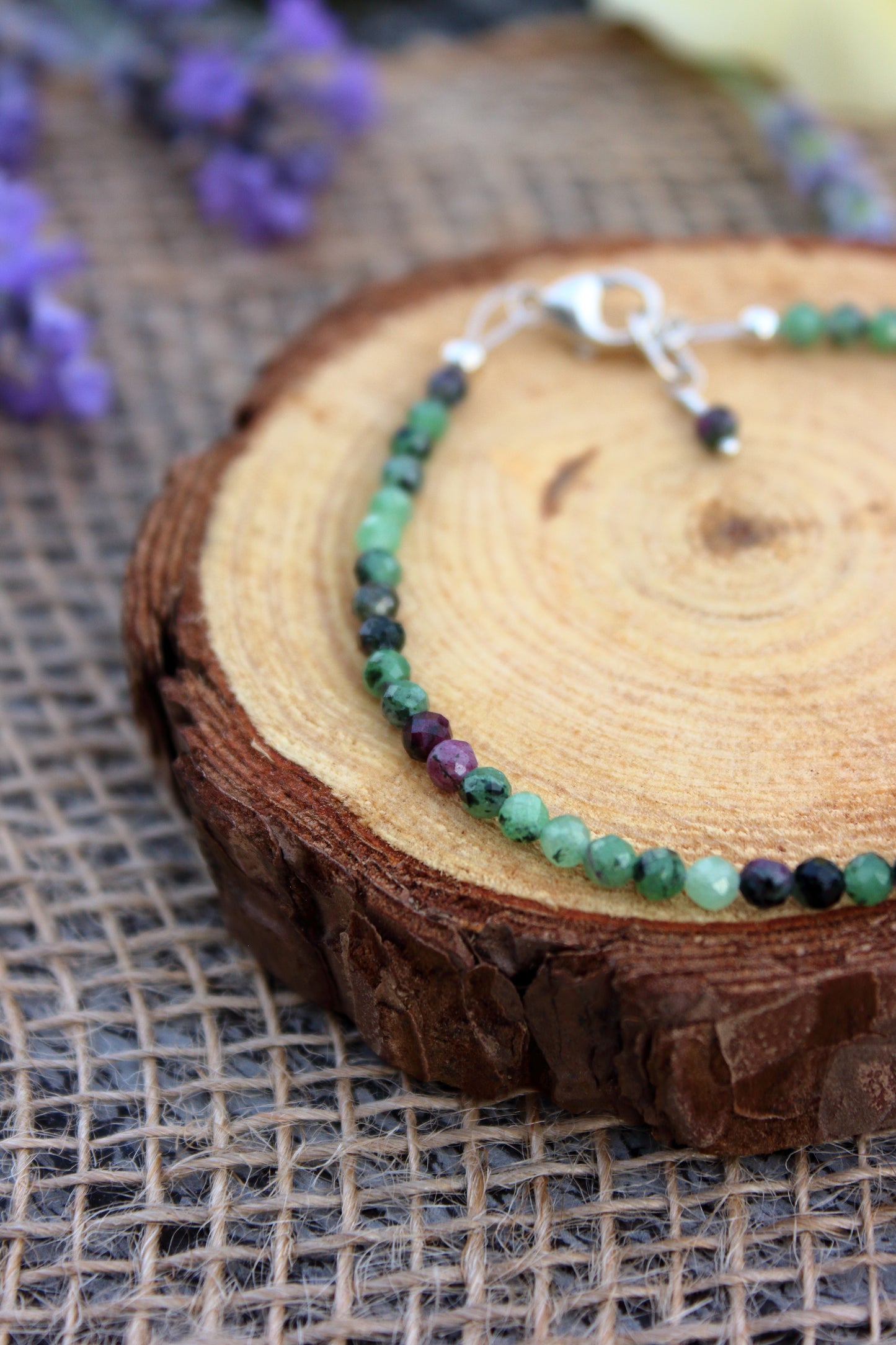 Bracelet with green and purple beads on a wooden surface with flowers in the background