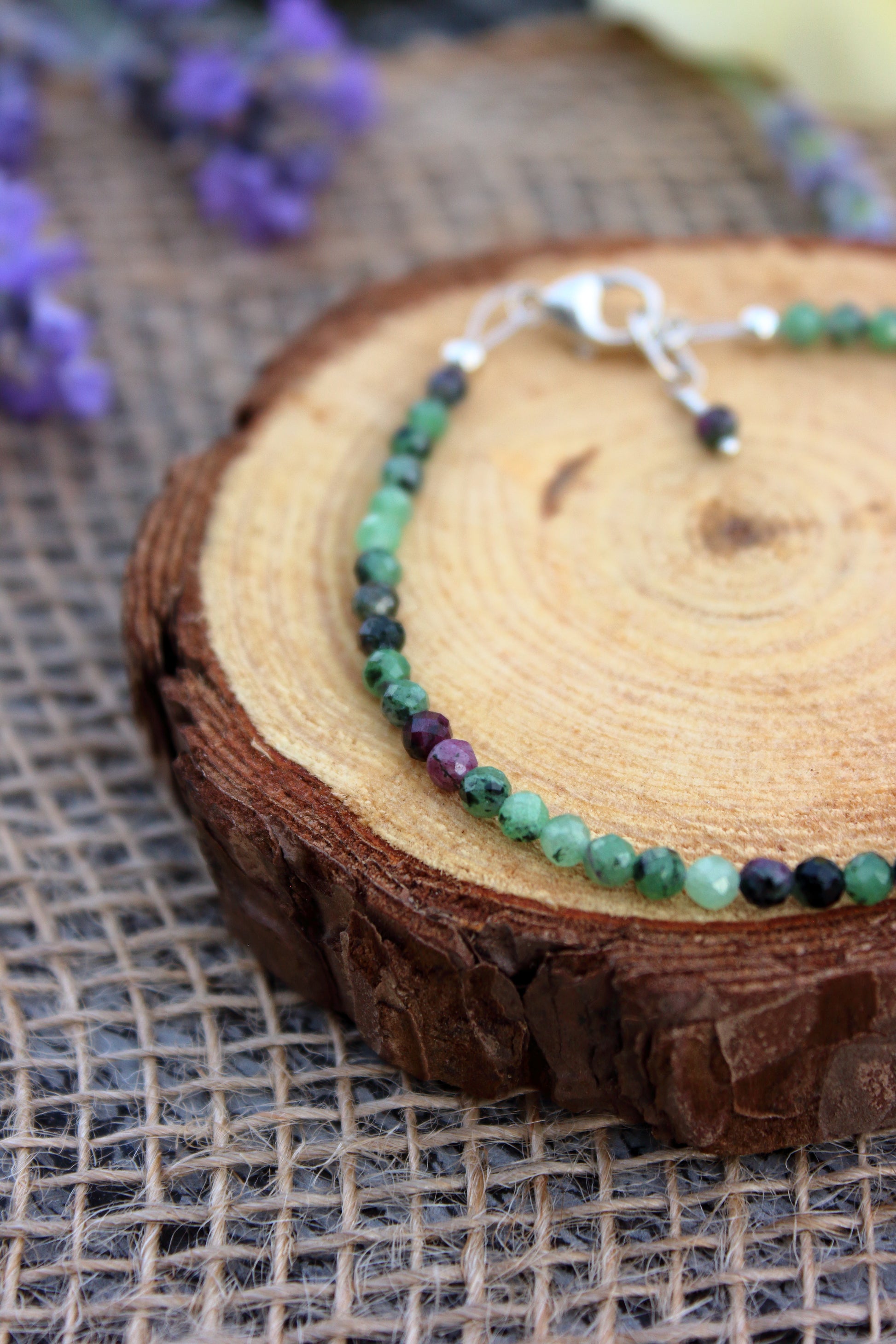 Bracelet with green and purple beads on a wooden surface with flowers in the background