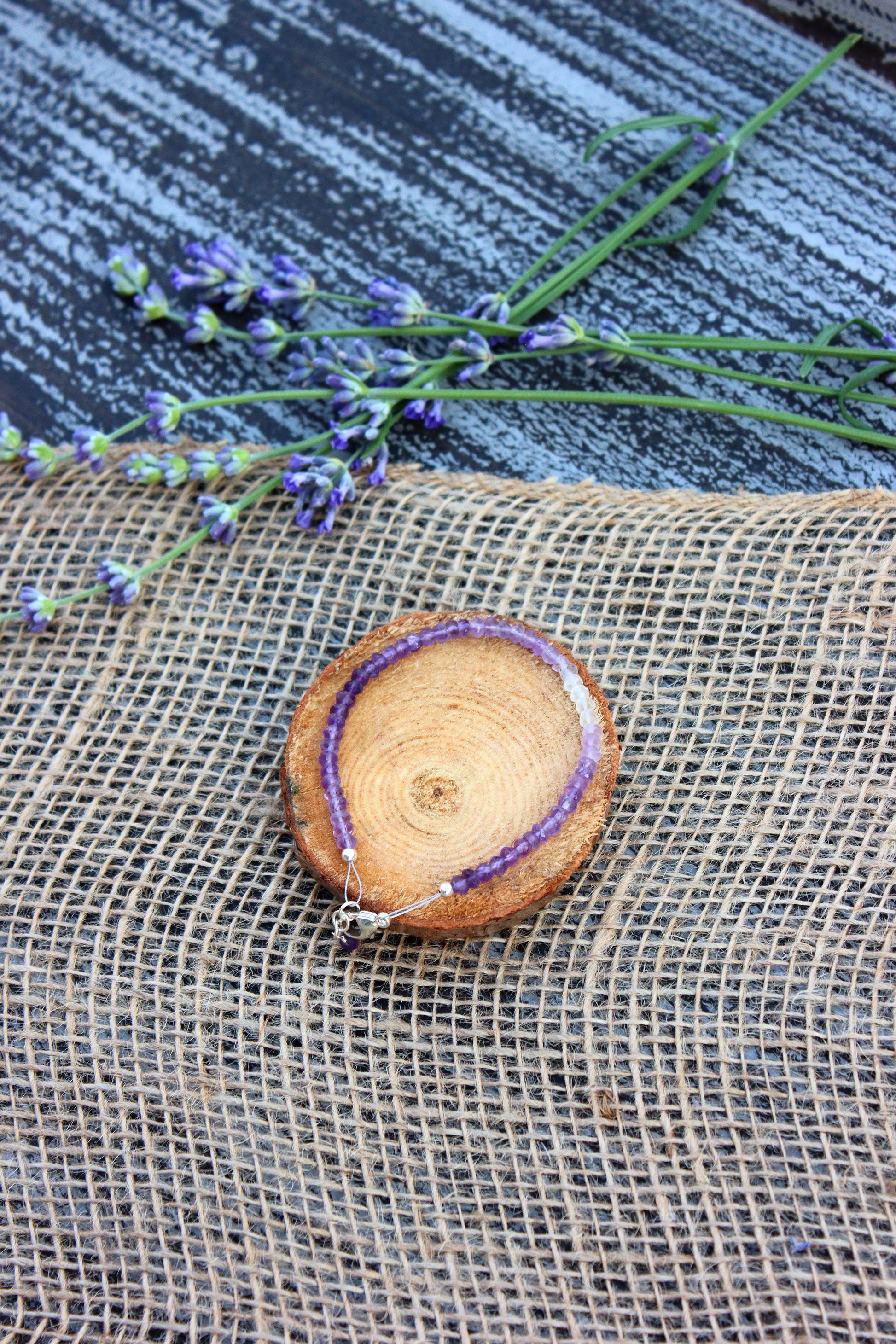 Purple beaded bracelet on a wooden disc with lavender flowers on a textured surface