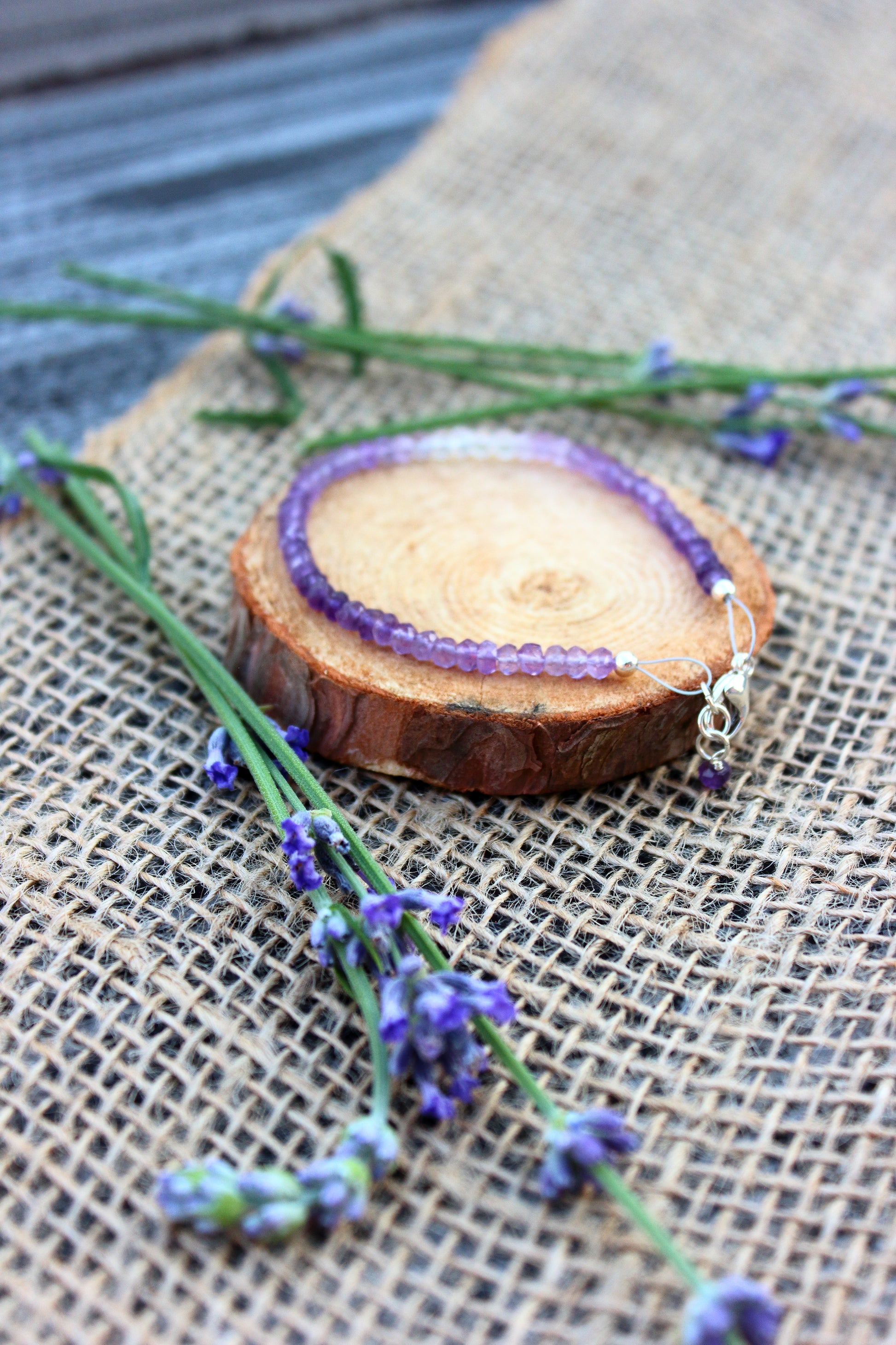 Amethyst beaded bracelet on a wooden slice with lavender flowers on a textured surface