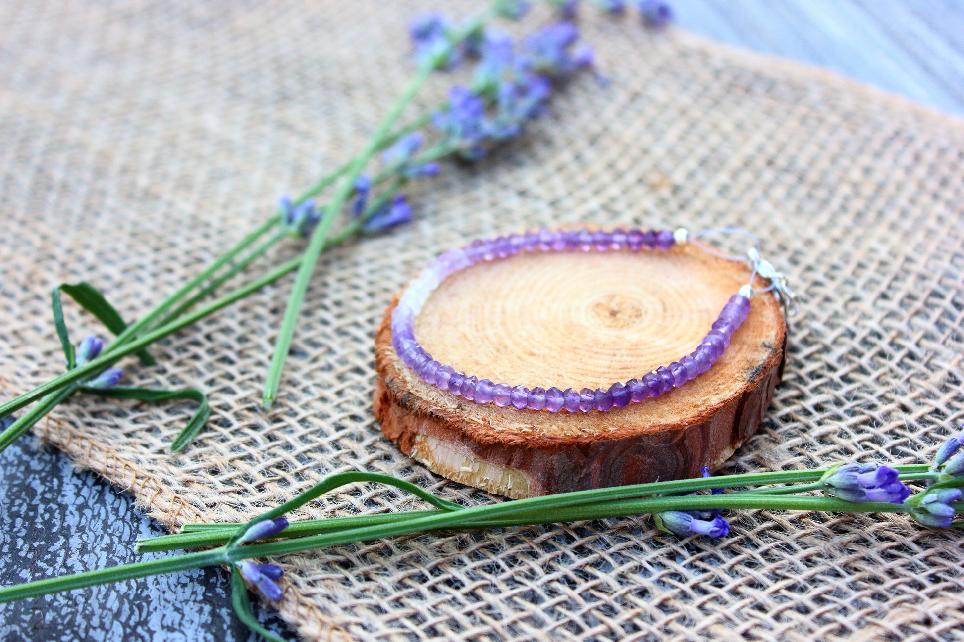 Purple beaded bracelet on a wooden block with lavender flowers on a textured surface