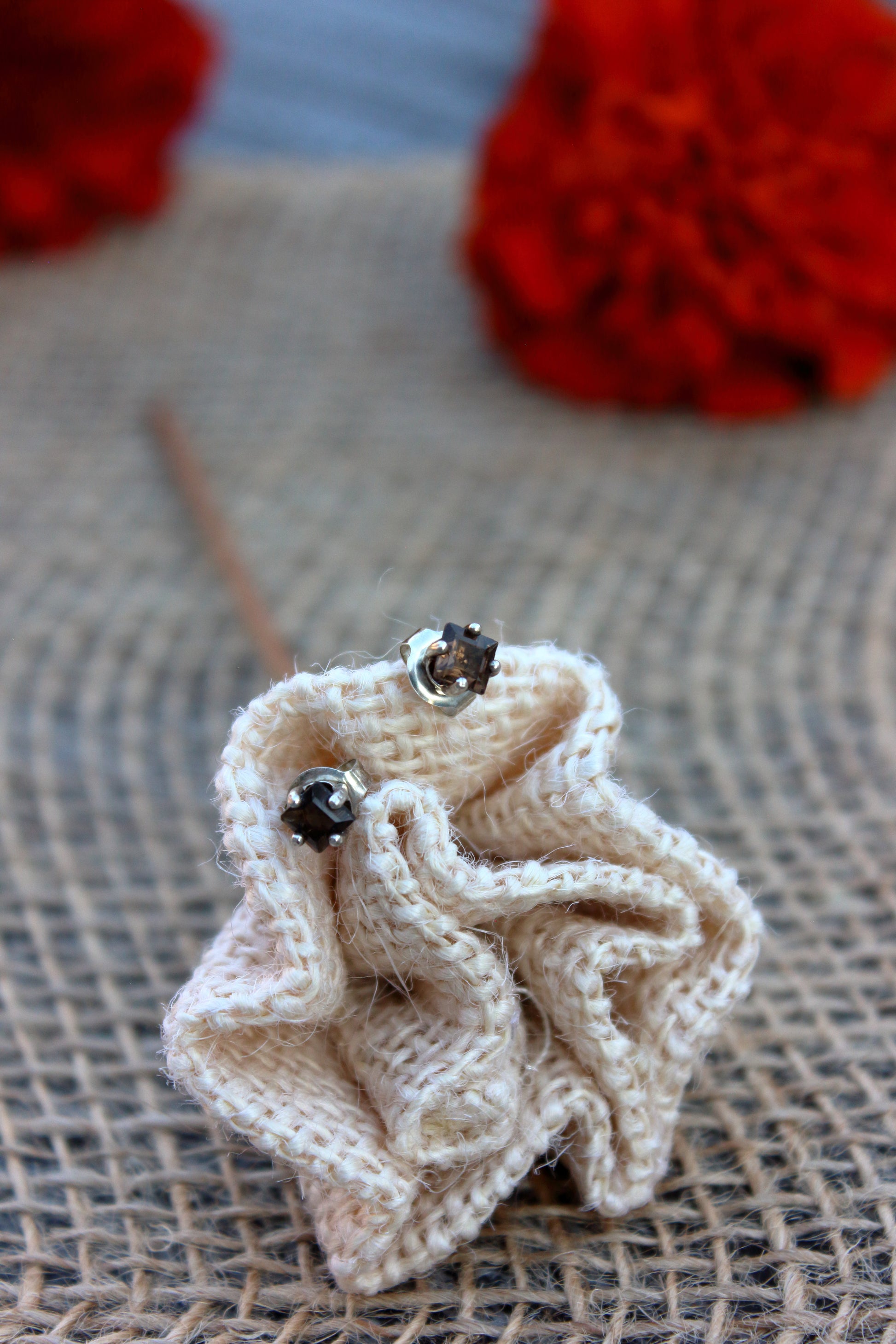 Knitted beige flower with silver studs on a textured surface with red flowers in the background