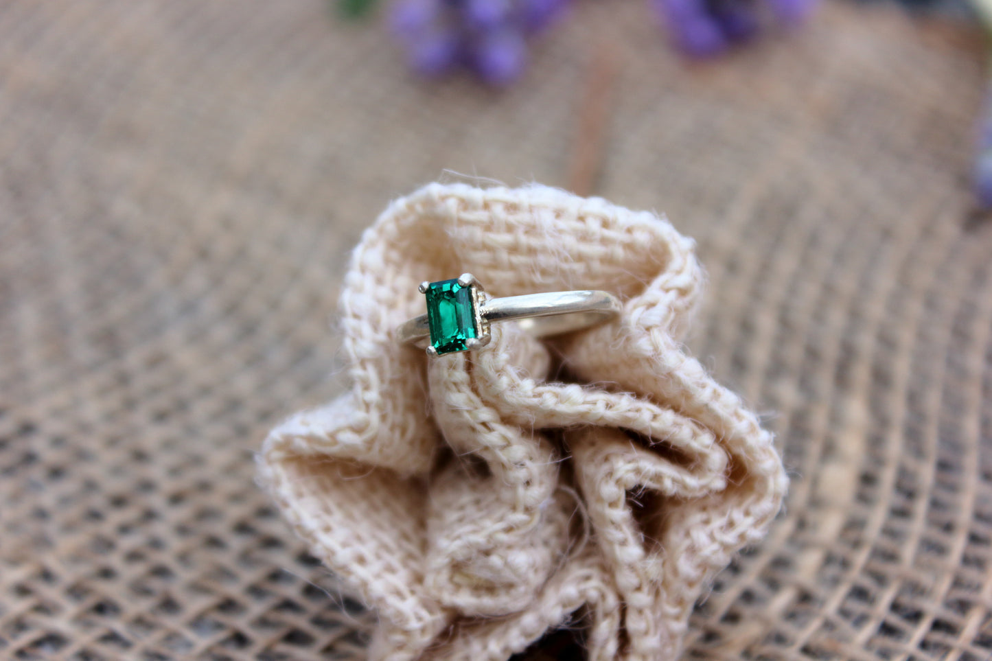 Ring with a green gemstone on a knitted fabric with a burlap background