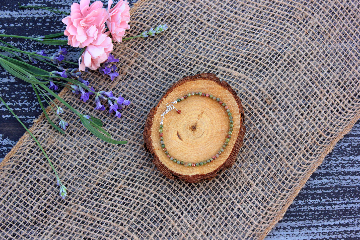 Bracelet on a wooden coaster with pink flowers and lavender on a textured surface
