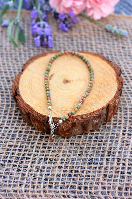 Beaded necklace on a wooden stump with flowers in the background