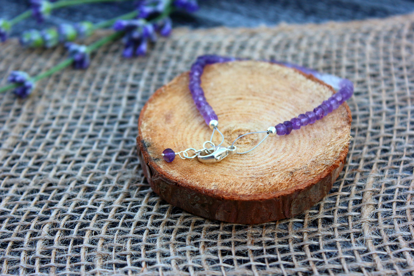 Purple beaded bracelet on a wooden block with lavender flowers in the background