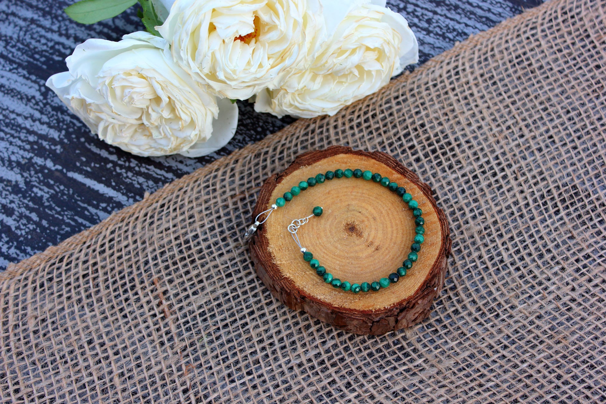 Green beaded bracelet on a wooden slice with white flowers in the background