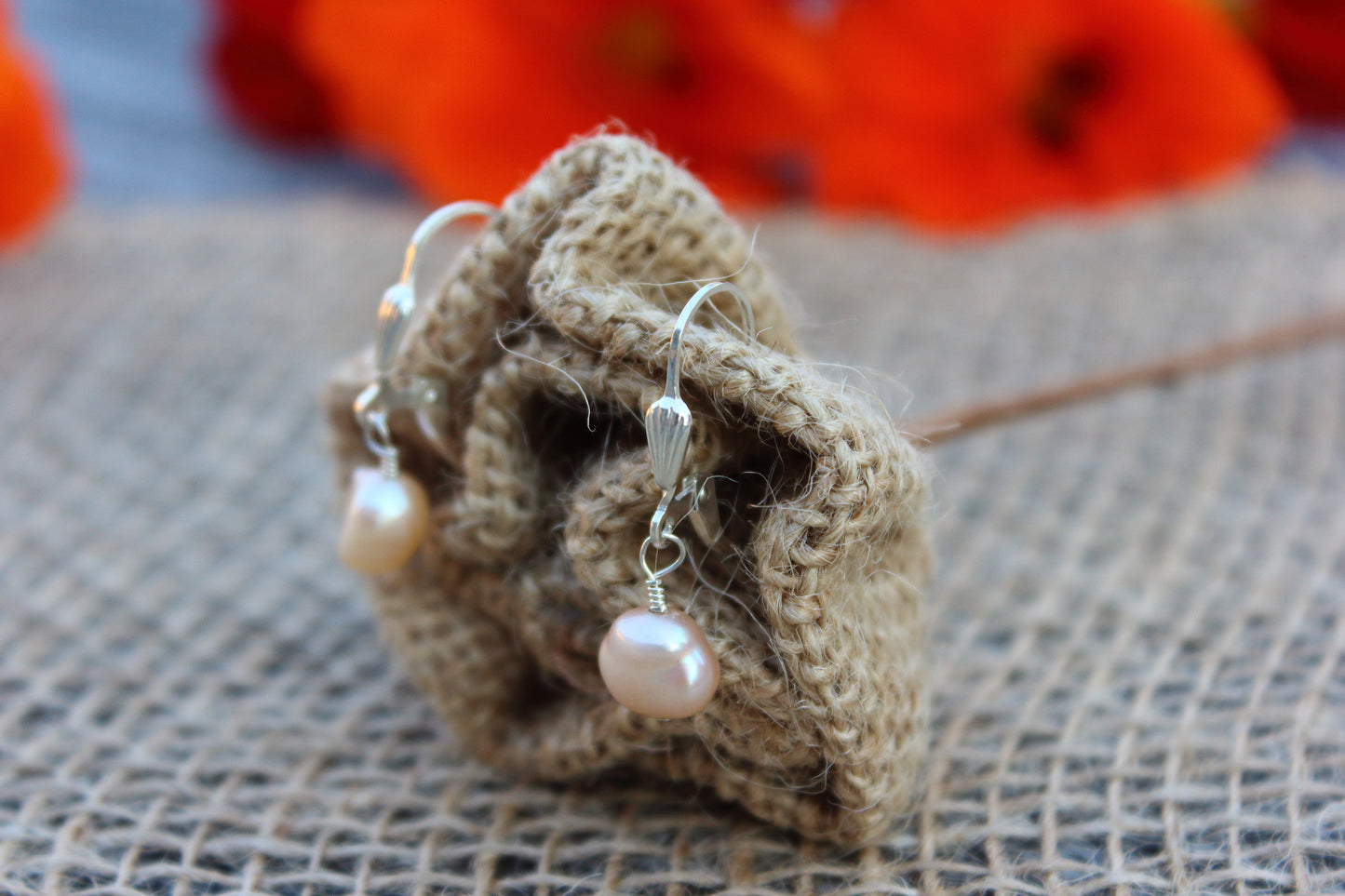 Pearl earrings on a textured surface with blurred red flowers in the background