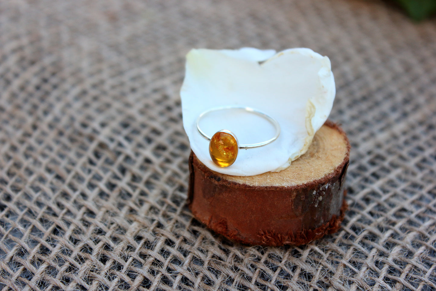 Ring with a yellow gemstone on a white stone and wooden block against a textured fabric background