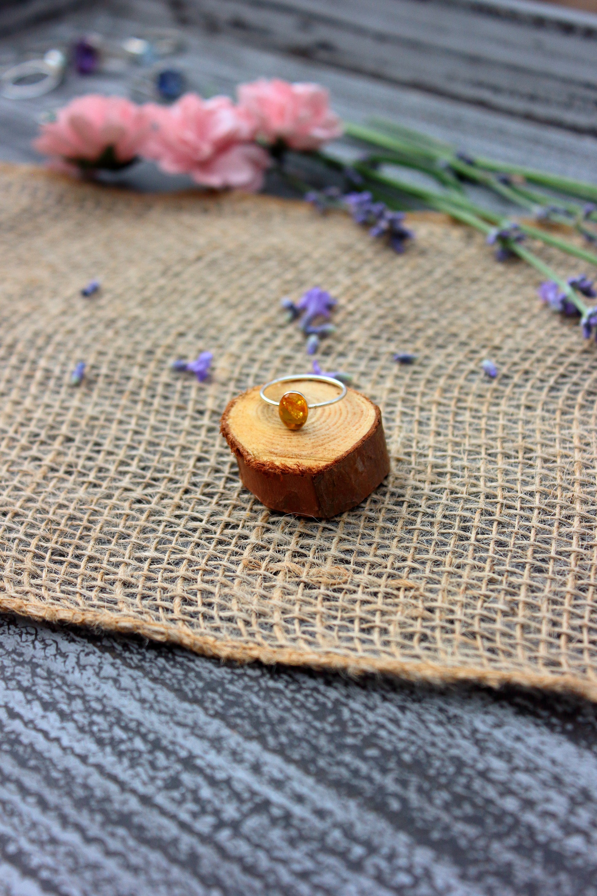 Ring with a yellow gemstone on a wooden block, surrounded by flowers on a textured surface